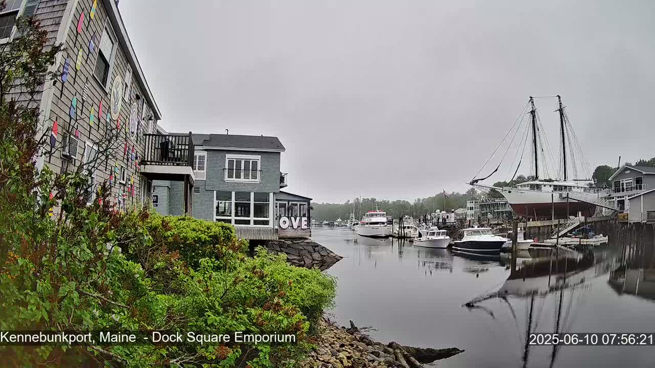 A harbor scene on an overcast day shows several boats, including a large sailing ship, docked near buildings with colorful decorations.