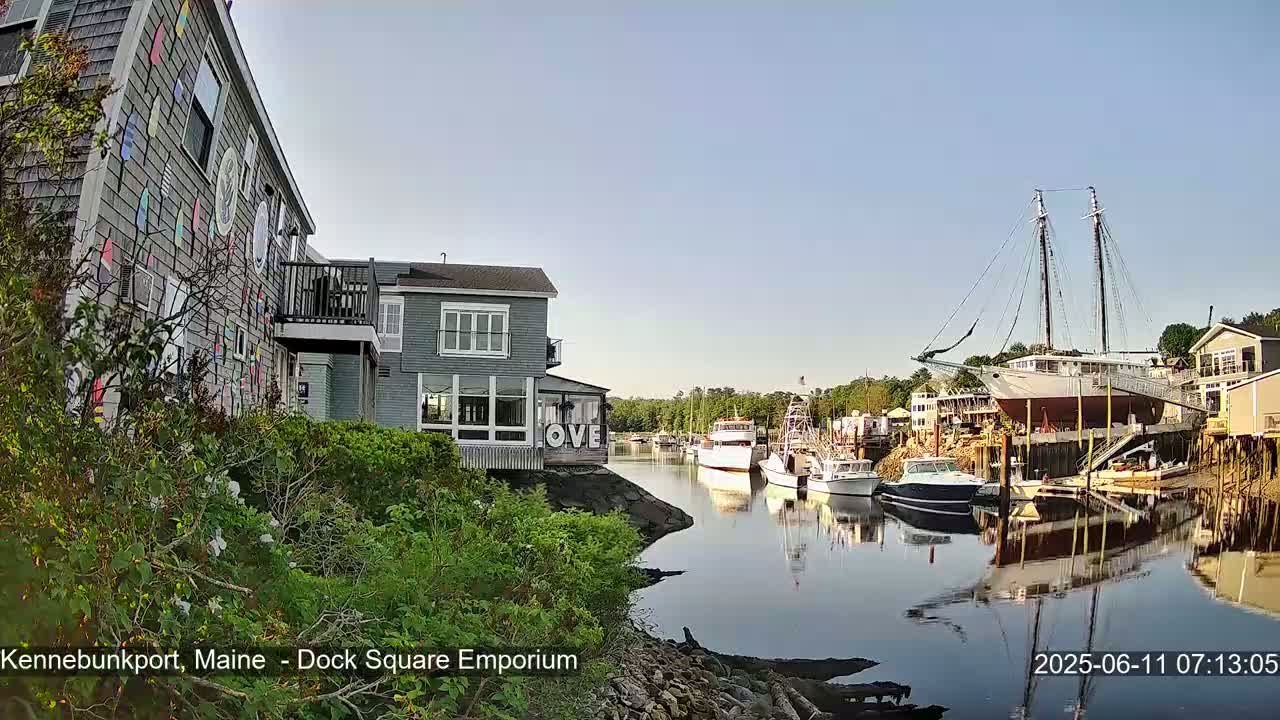A calm, sunny day at a waterfront harbor shows several boats docked, including a large sailing ship, near buildings with colorful exterior decorations.