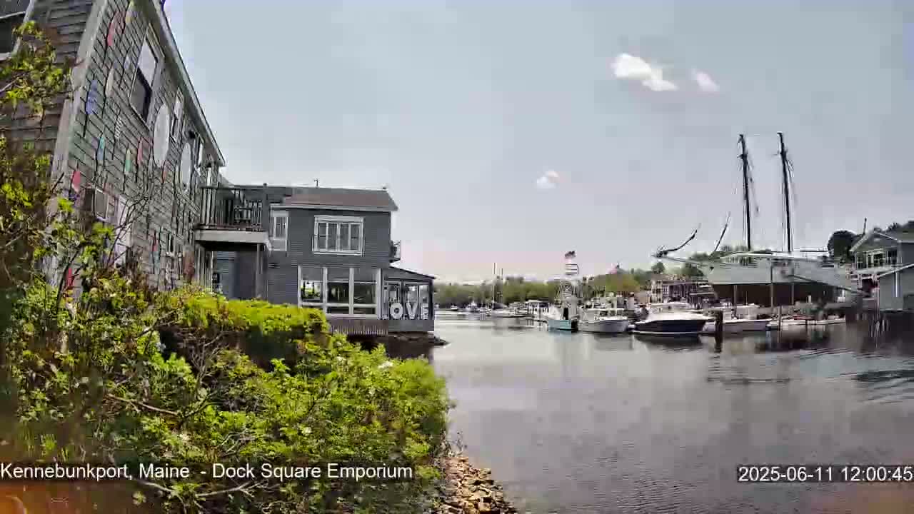 A calm waterway with several boats docked, including a large sailing vessel, is seen beside buildings, one of which displays large letters spelling "LOVE," under a partly cloudy sky.