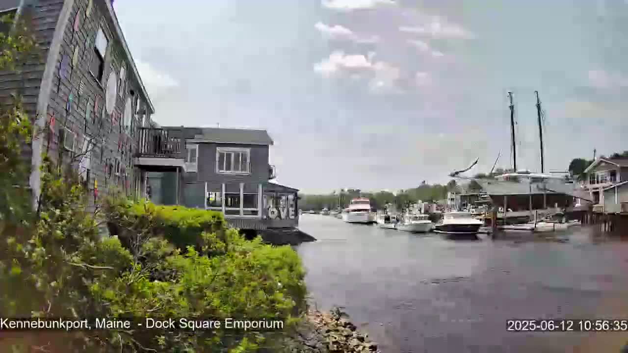 A partly cloudy day shows a harbor with several boats docked, including a large sailboat, and buildings along the waterfront, one of which has "LOVE" displayed on its side.