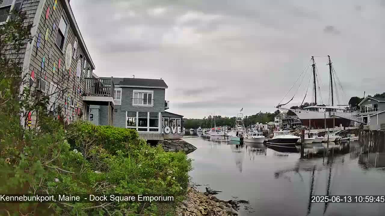 A calm harbor scene on an overcast day shows several boats docked near a building with colorful decorations on its exterior.