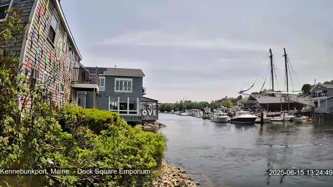 A calm waterway with docked boats and buildings, one of which has colorful artwork on its side, under a mostly cloudy sky.