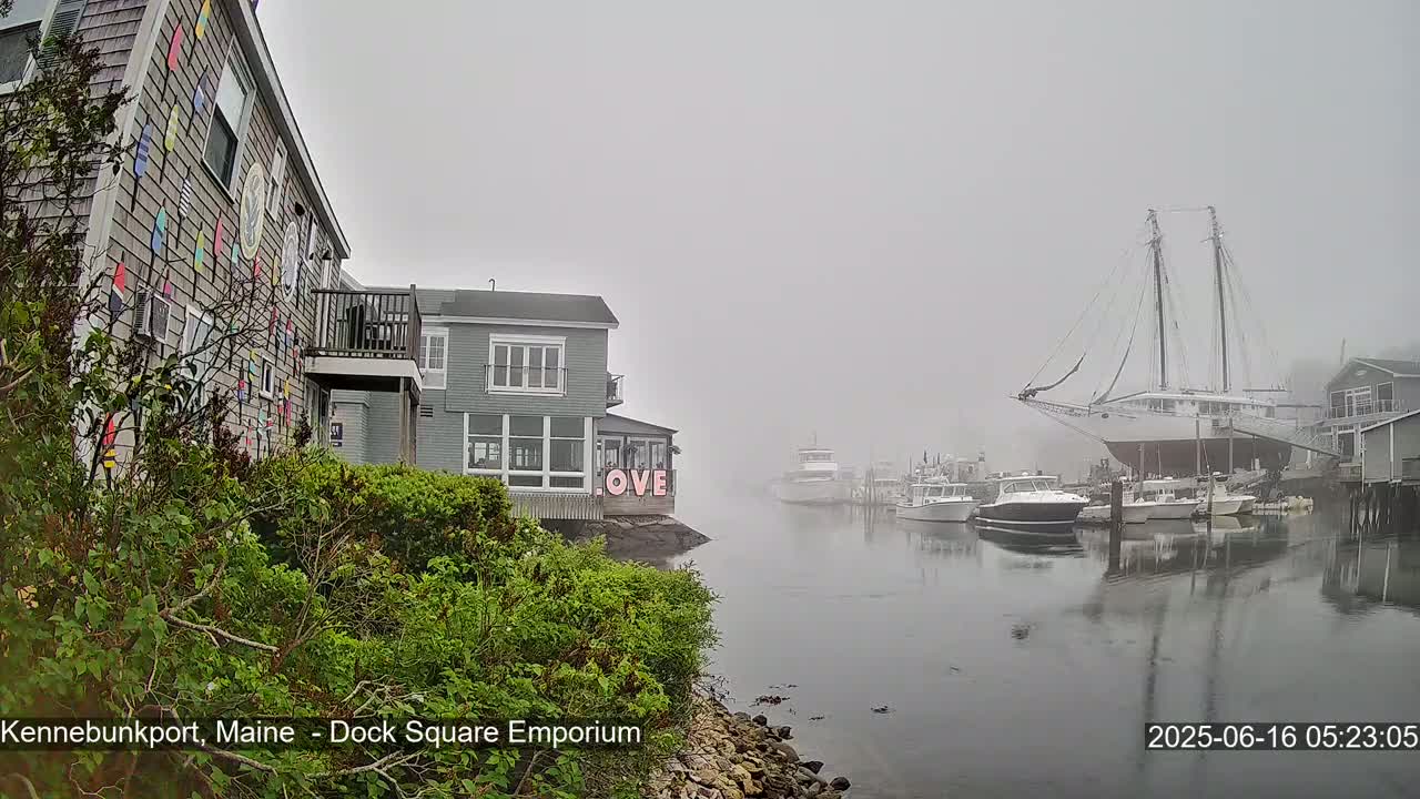 A foggy harbor scene shows several boats, including a large sailboat on land, and buildings, one of which has a colorful exterior.