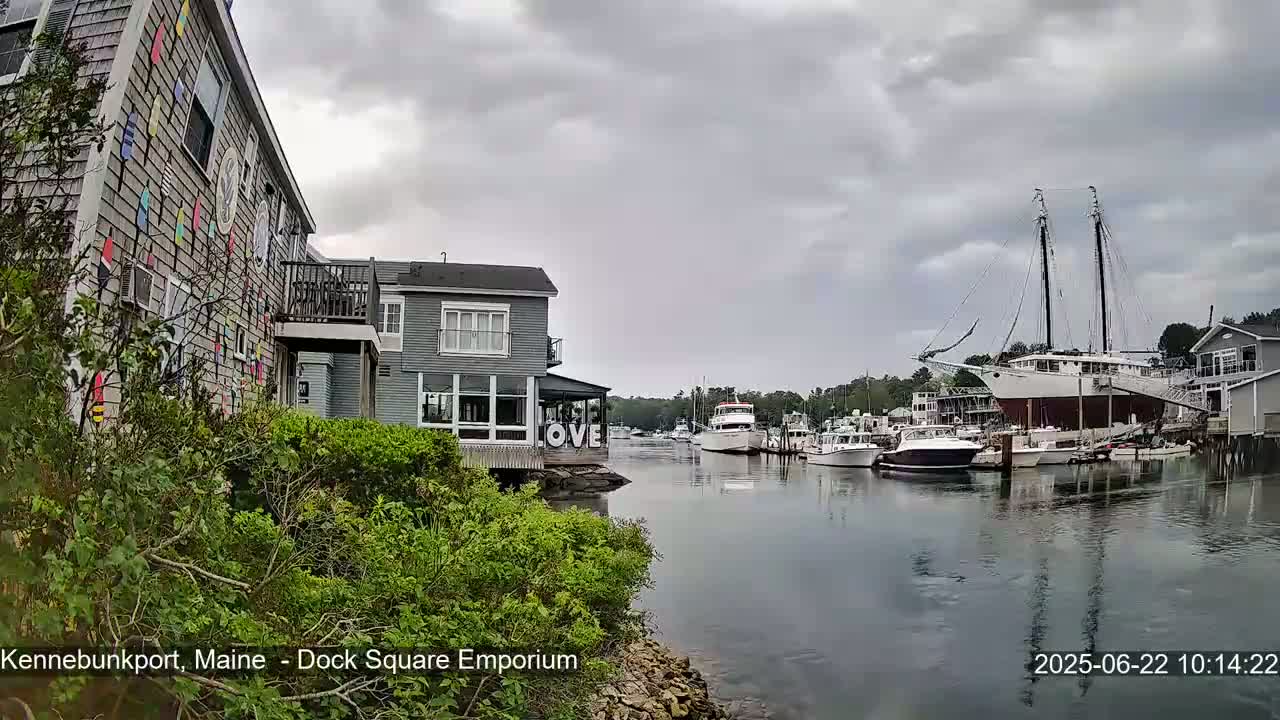 A harbor scene under an overcast sky shows several boats docked, including a large sailing ship, near buildings with colorful exterior details.