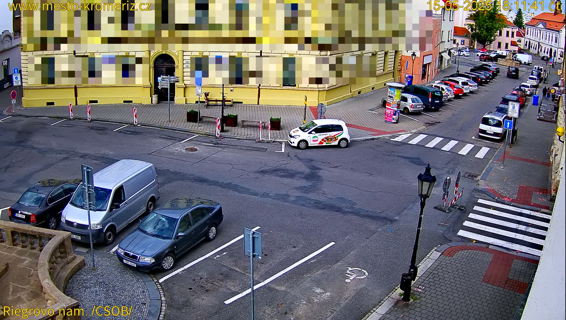 A street scene shows several parked cars, a van, and a small white car on a mostly empty city street under an overcast sky.