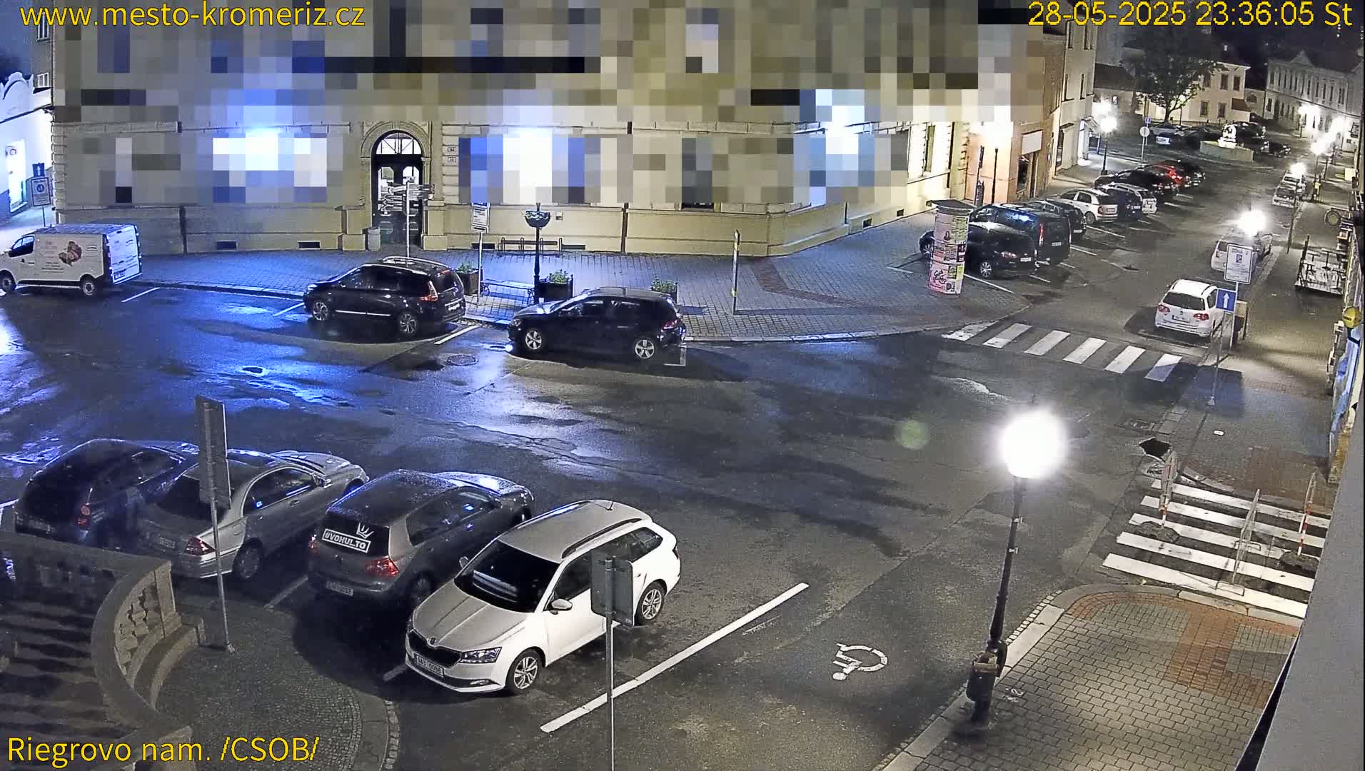 Several cars are parked on a wet, nighttime street in front of a building.