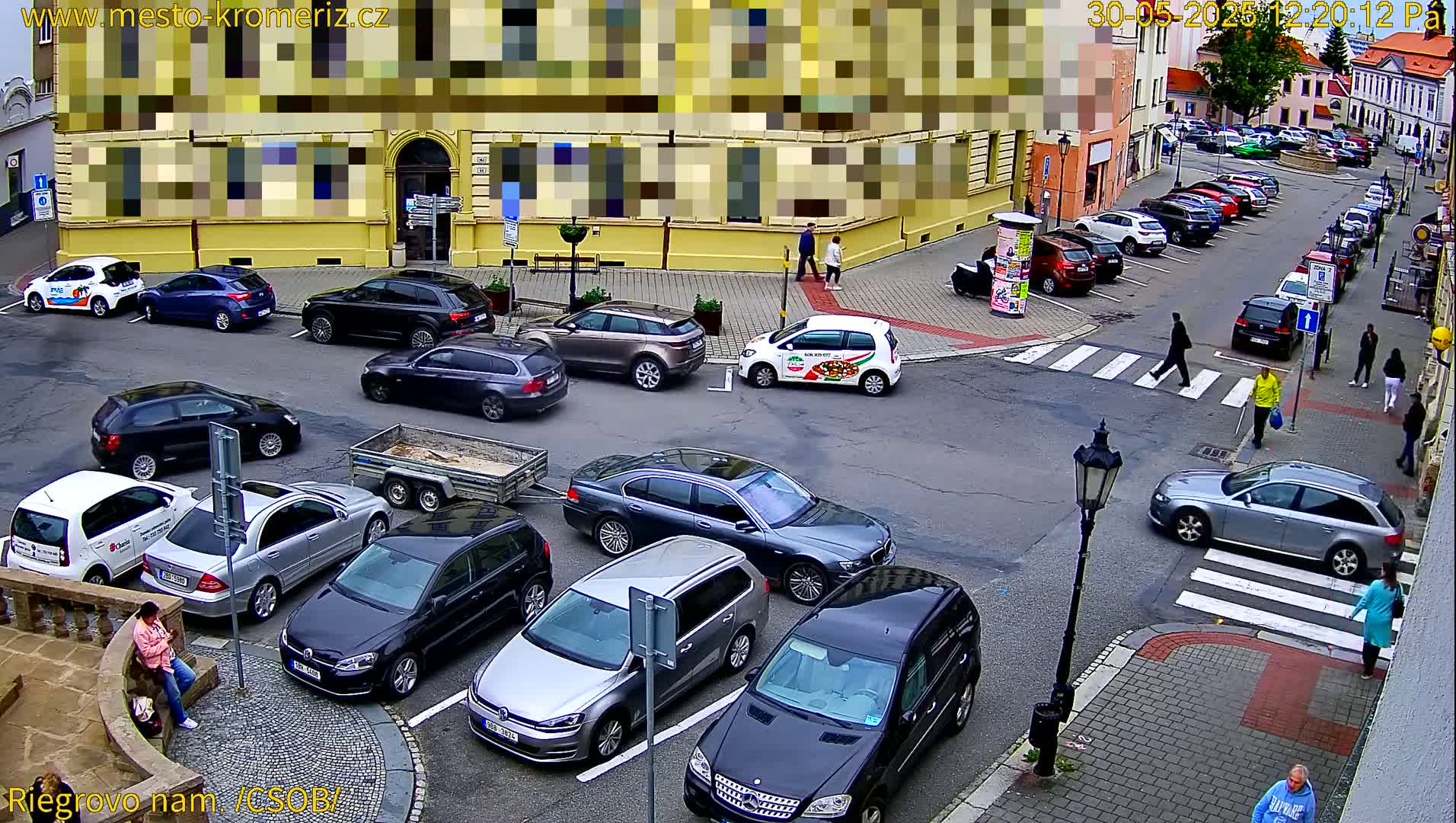 A city square with many parked cars and a few pedestrians, viewed from above on an overcast day.