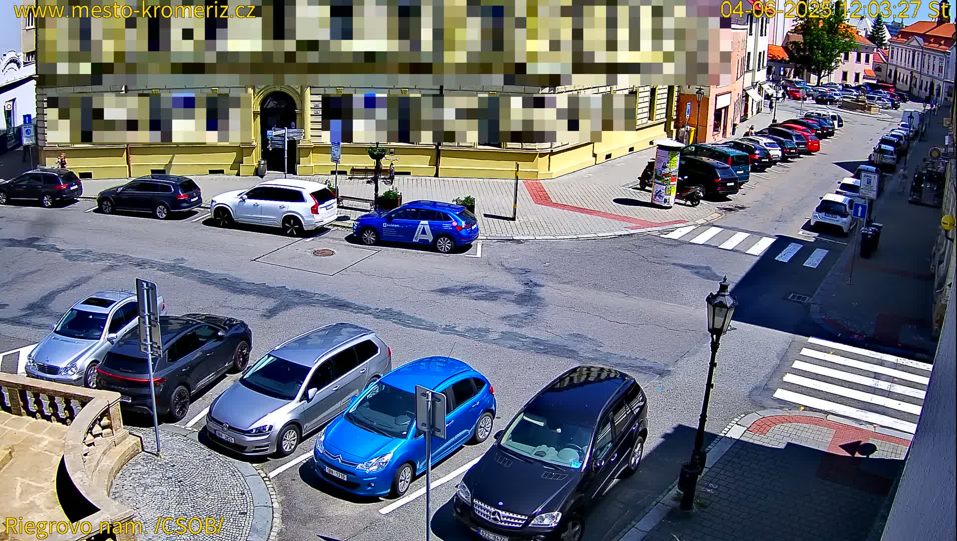 A sunny day reveals a street corner with parked cars, a crosswalk, and a building partially obscured.