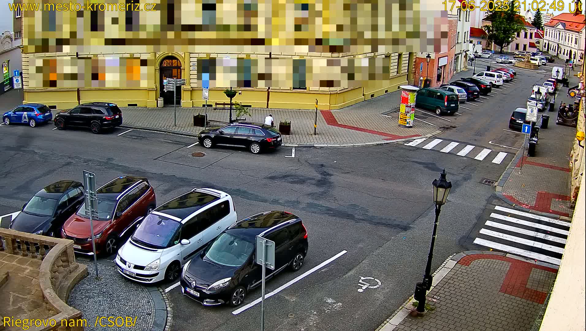 Several cars are parked in a city parking lot on a partly cloudy day.