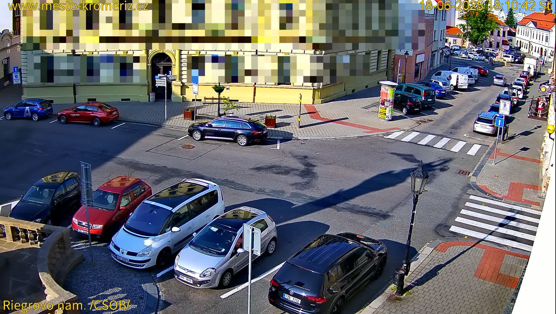 Several cars are parked in a street-side lot next to a crosswalk on a sunny day.