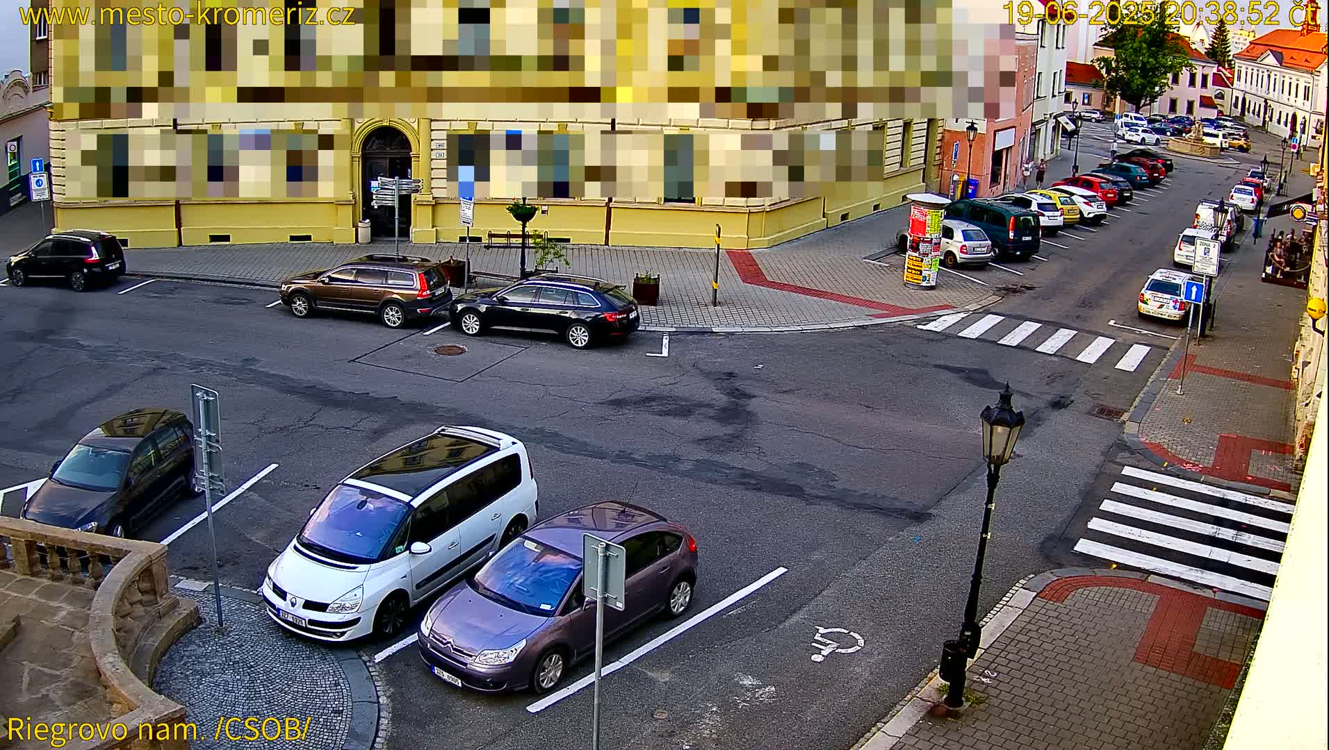 A street-level view of a parking lot and street intersection with several cars parked, under a partly cloudy sky.