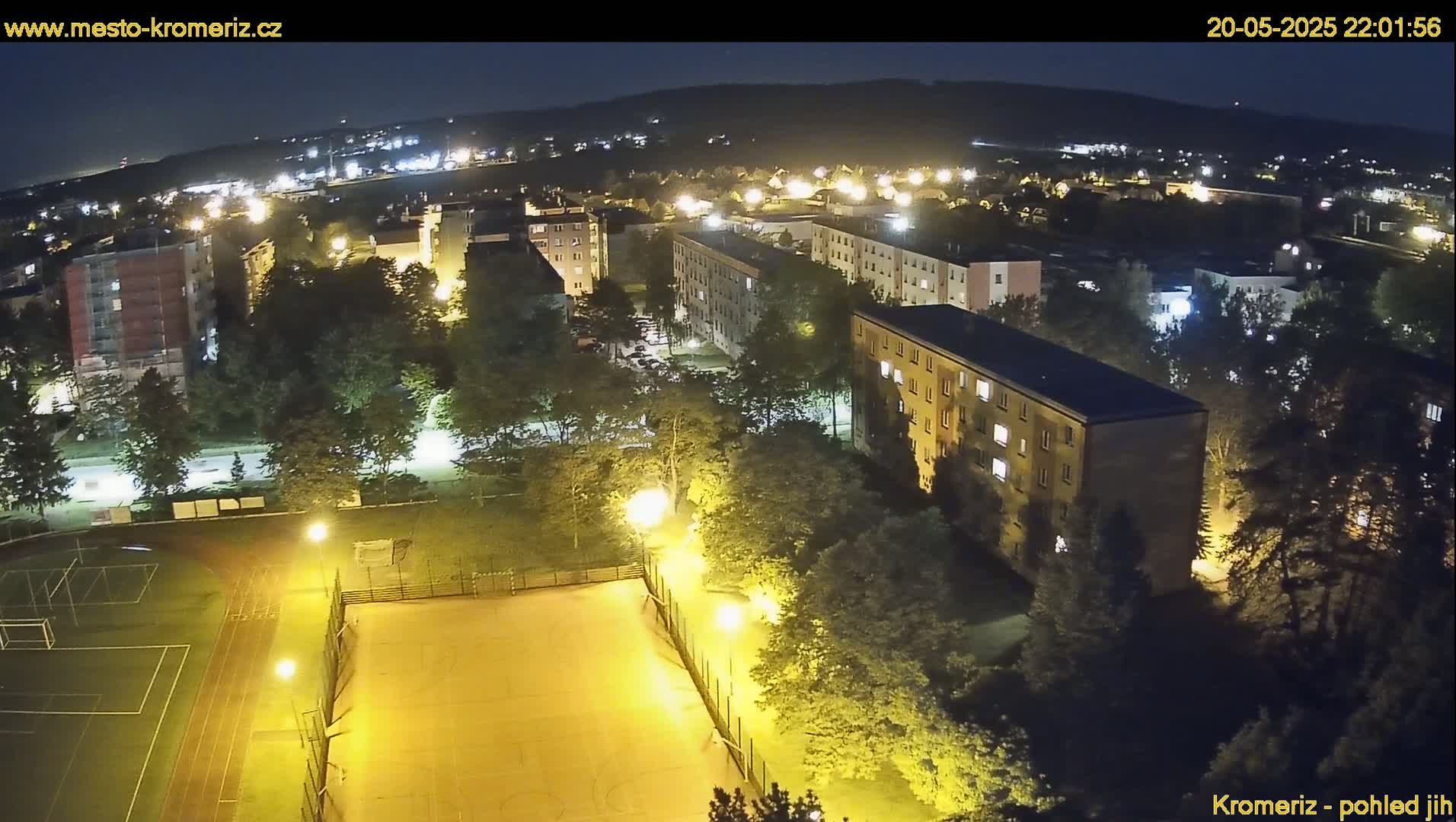 A nighttime aerial view of a residential area with illuminated buildings, trees, and a sports field.