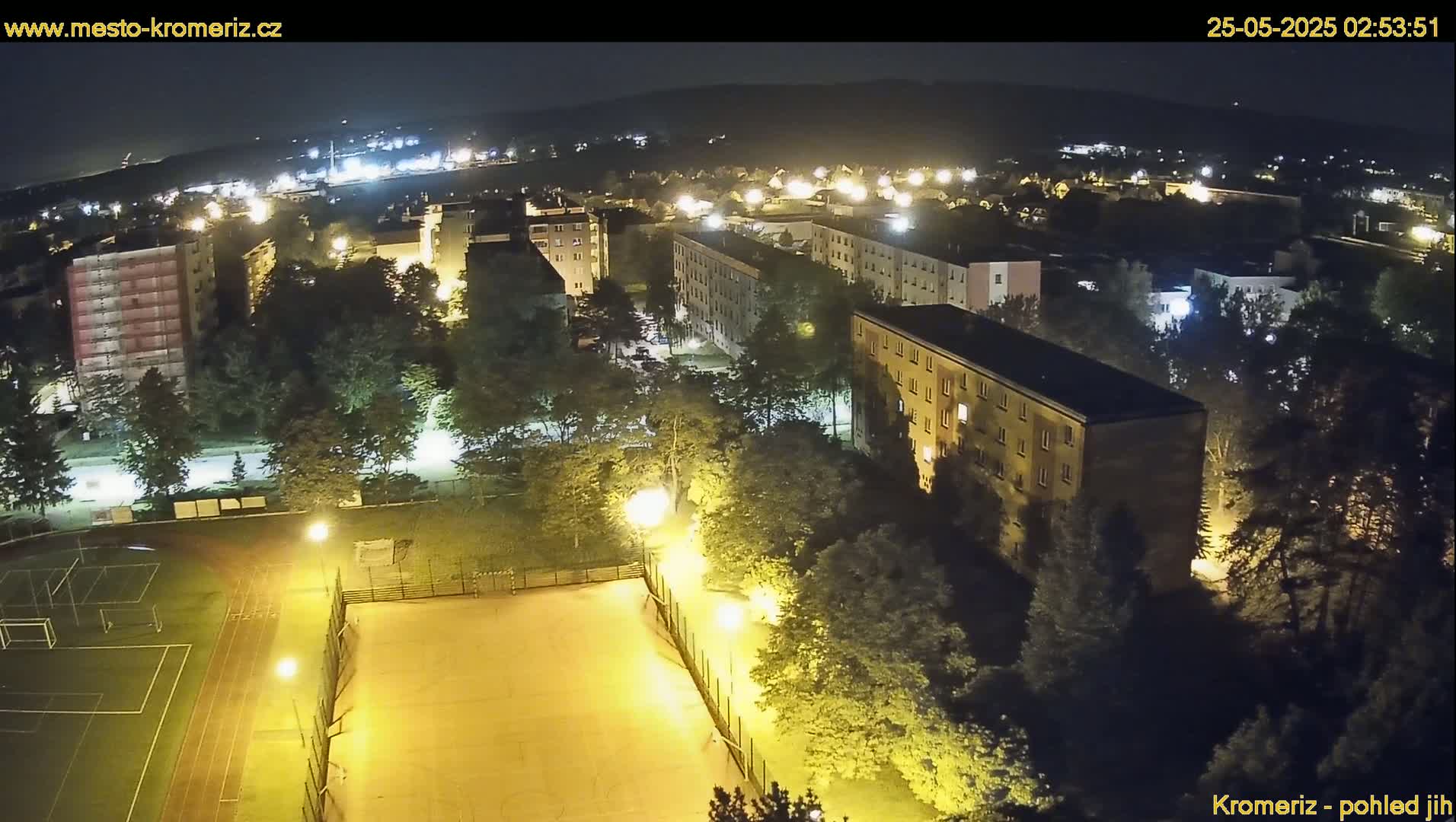 A nighttime aerial view of a residential area with a sports field illuminated by artificial lights.