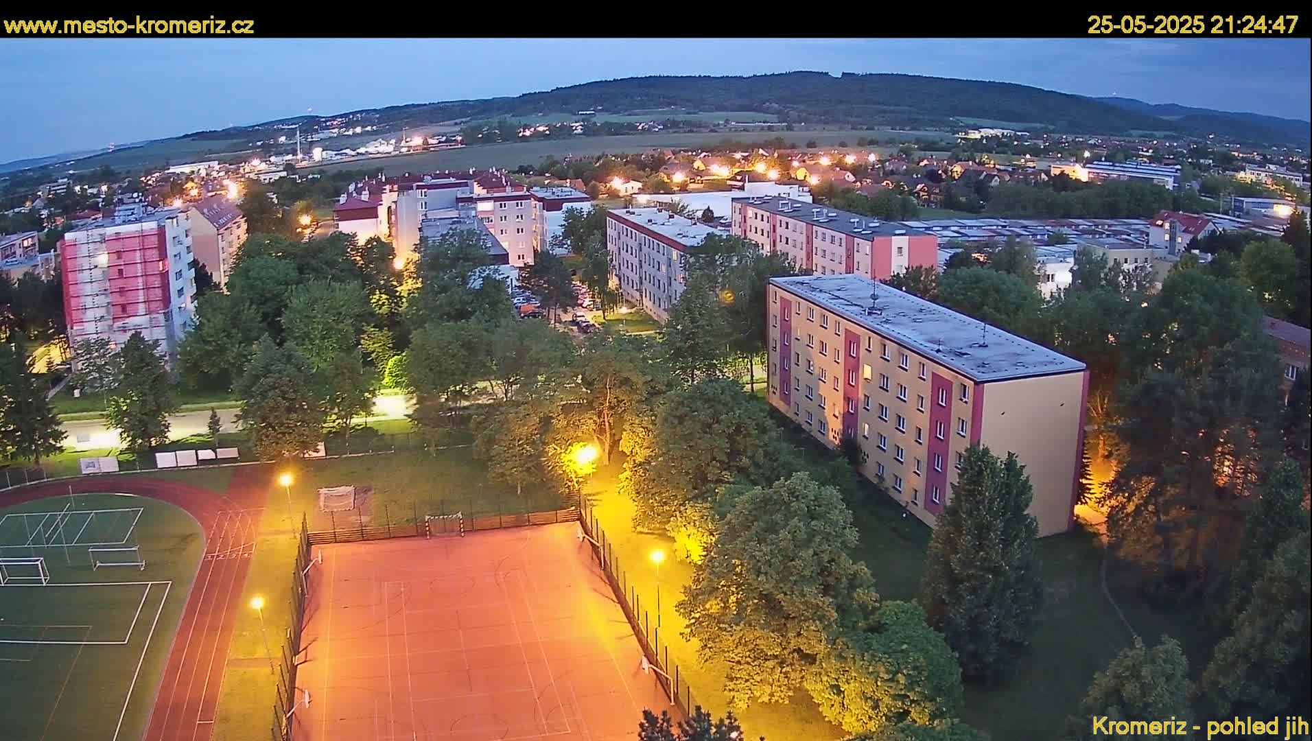 An aerial evening view of a residential area with illuminated sports fields and apartment buildings under a twilight sky.