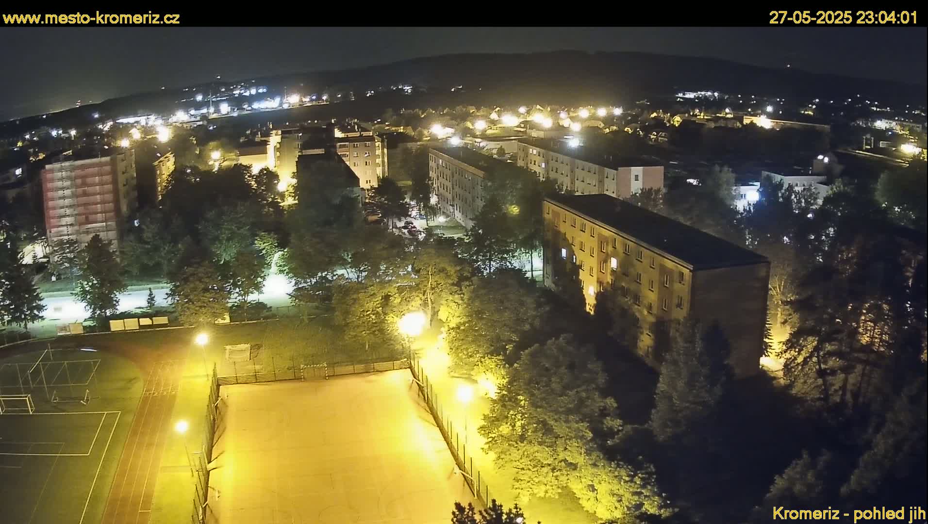 A nighttime aerial view of a residential area with a sports field illuminated by artificial lights, under a clear sky.
