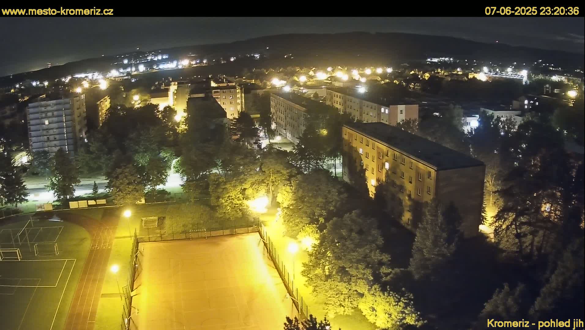 A nighttime aerial view of a residential area with a sports field, illuminated by streetlights under a clear, dark sky.