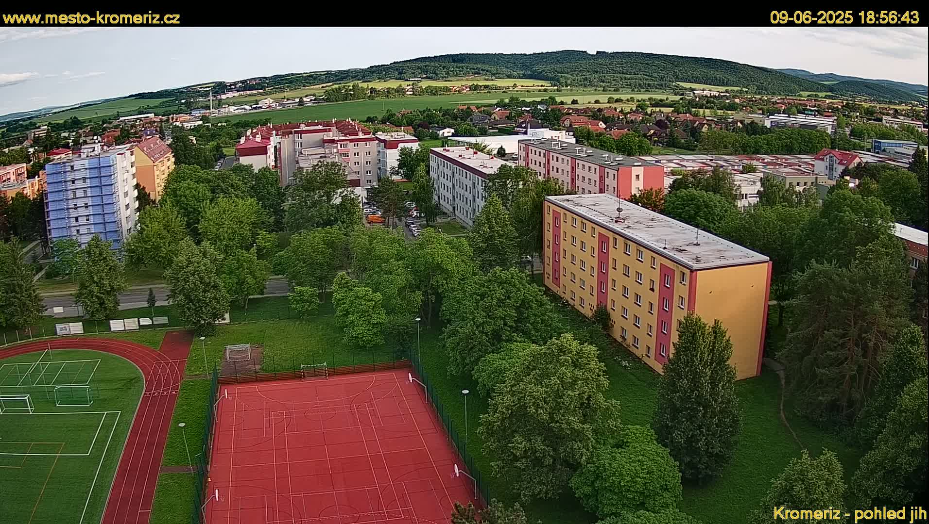 An aerial view of an apartment complex and a school playground, under a partly cloudy sky.