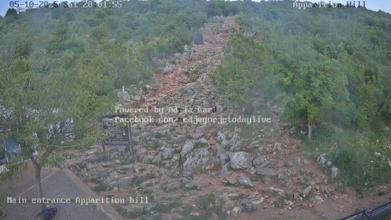 A rocky, uphill path winds through a hazy, green hillside.