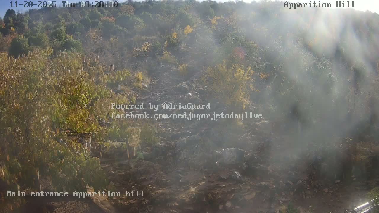 A rocky, sparsely vegetated hillside is visible under hazy daytime conditions, with an uneven path winding through the terrain.