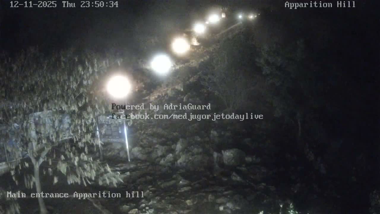 A rocky path winds up a dark hill at night, illuminated by a string of bright lights under clear skies.