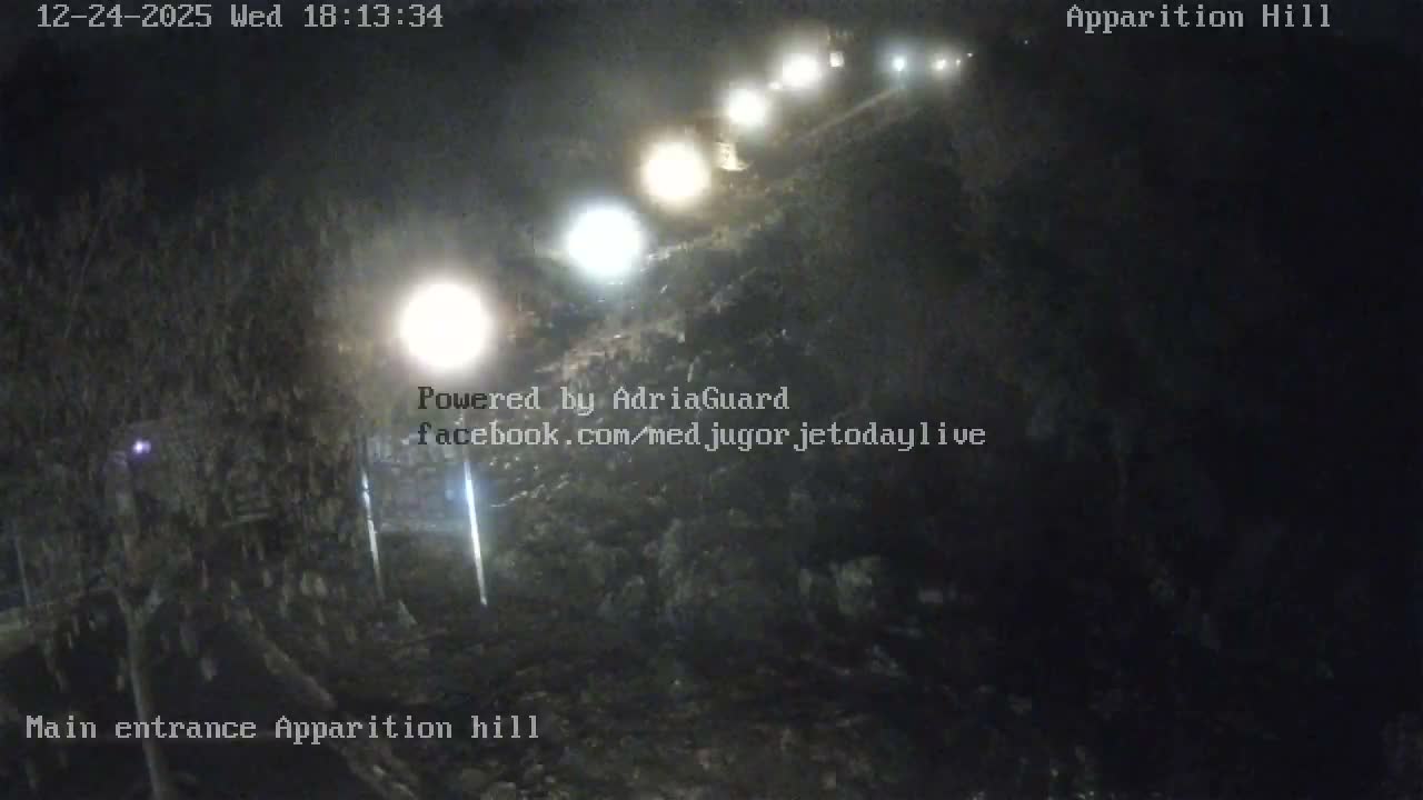 A rocky path winds up a dark hill at night, illuminated by a string of bright lights under clear skies.