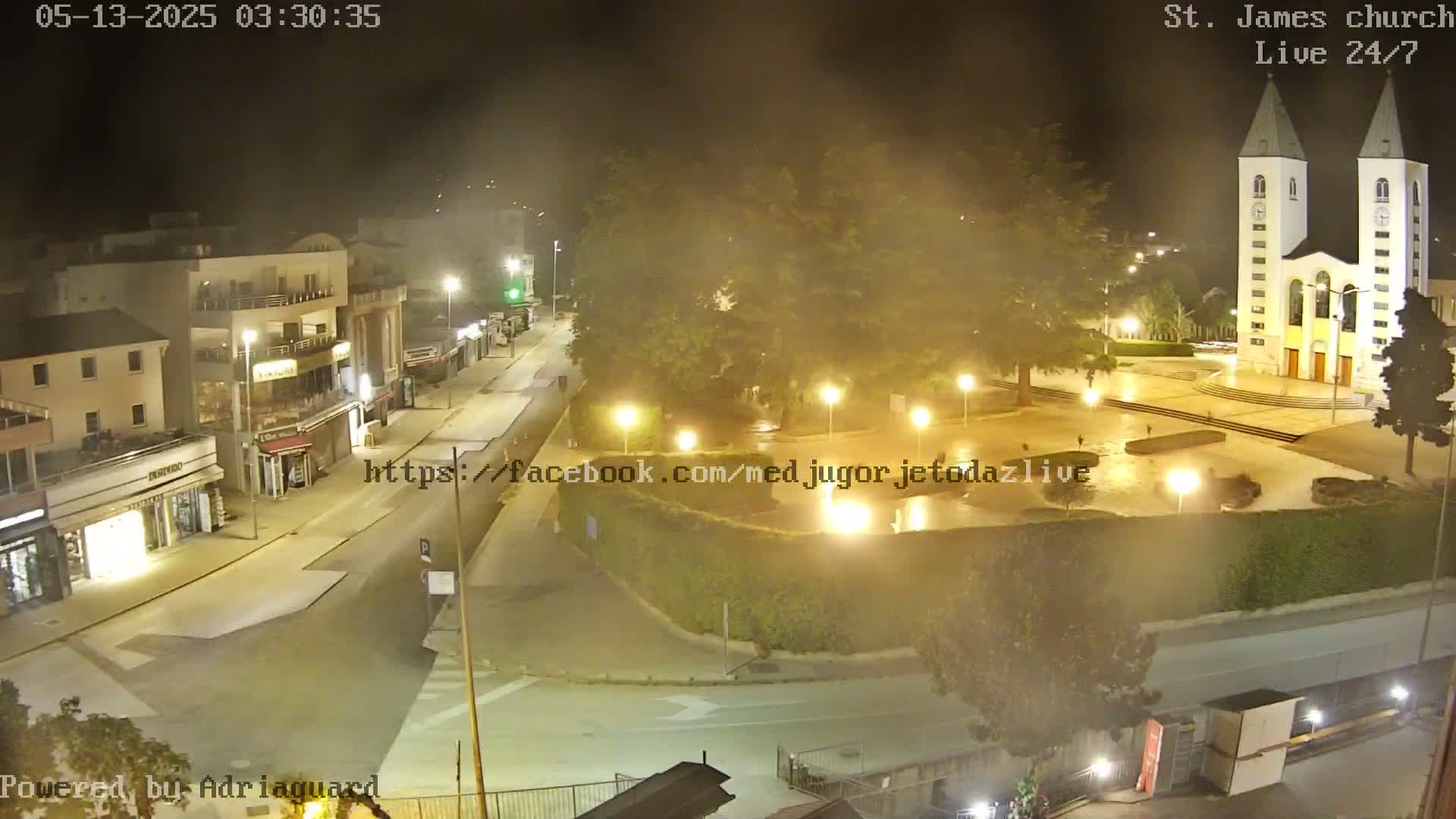 A nighttime aerial view of a town square with a church, buildings, and streets, under hazy conditions.