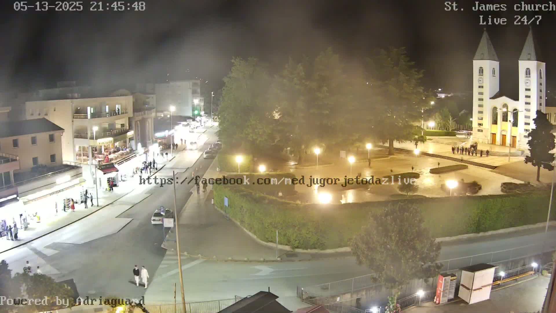 A nighttime, hazy view of a town square with a church, buildings, and people walking around.