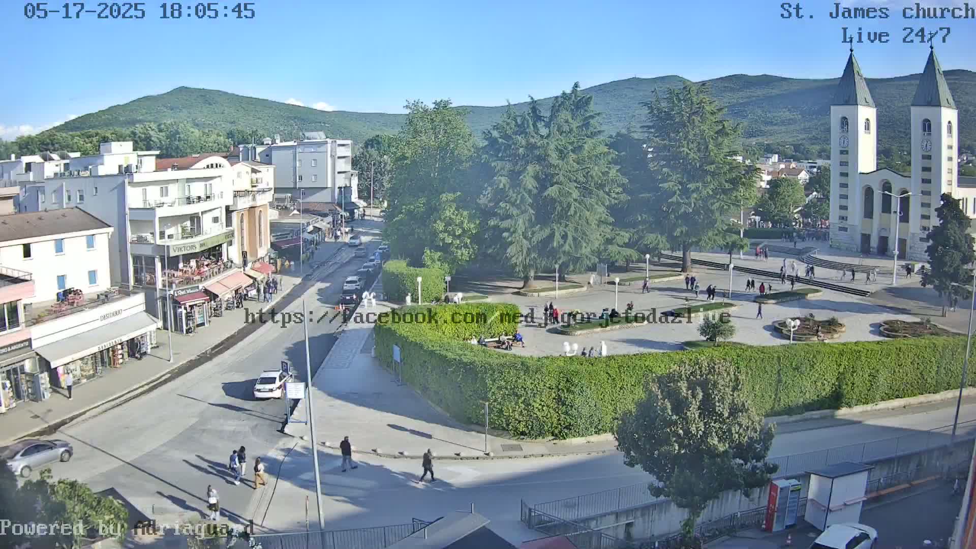 A town square with a large church, surrounded by buildings and greenery, on a sunny day.