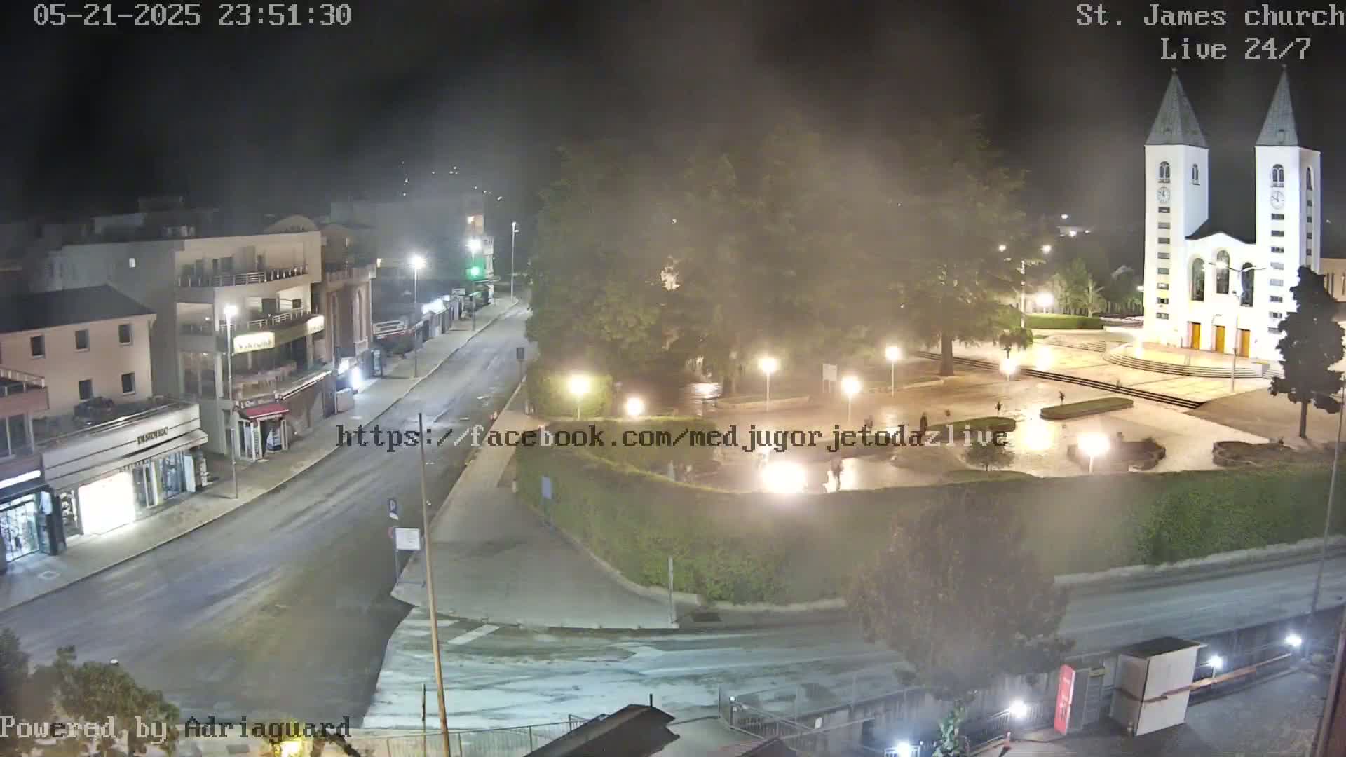 A nighttime, misty view of a town square with a church and several buildings, along with a mostly empty street.