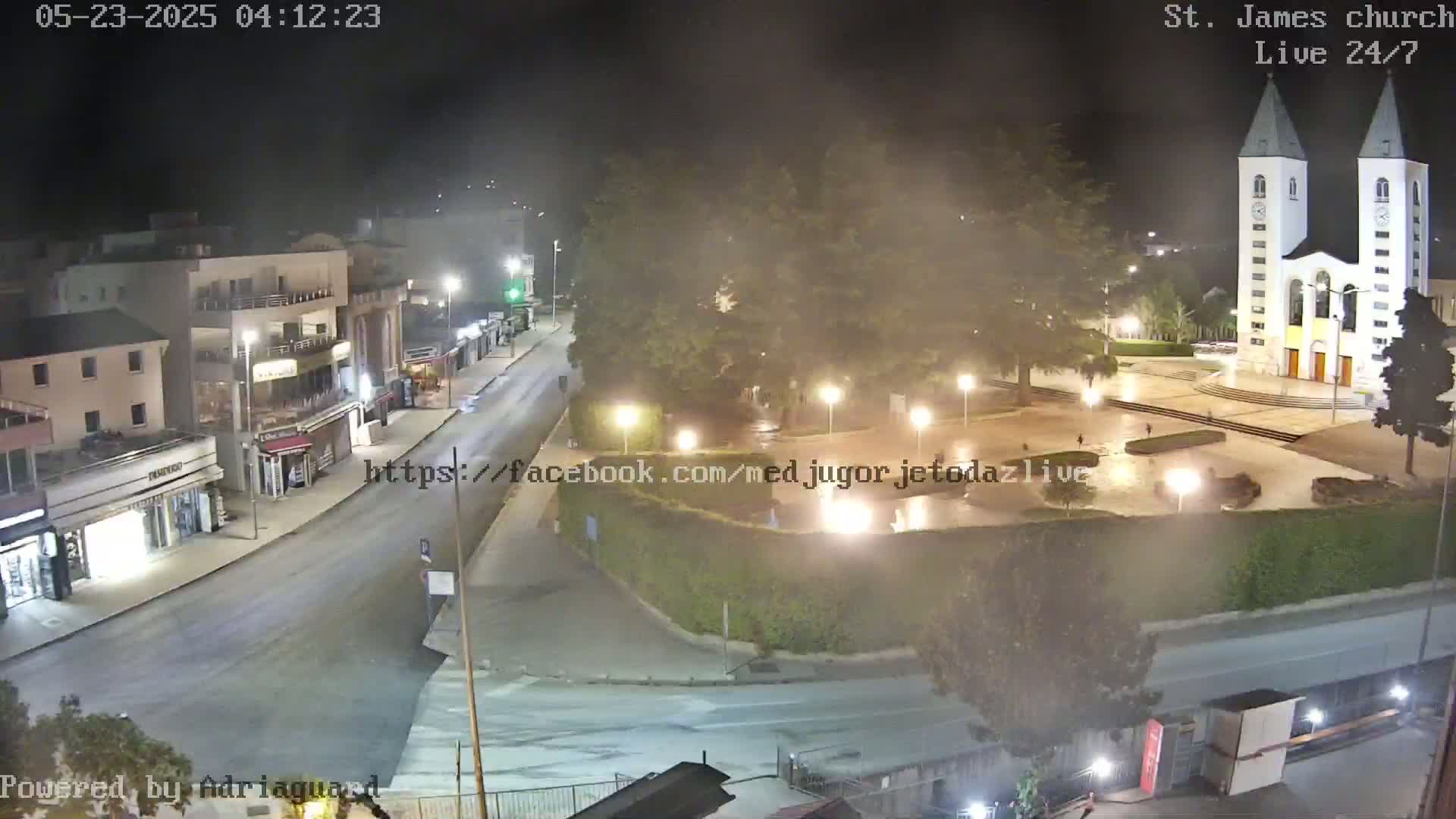 A nighttime, hazy view of a town square with a church, streetlights illuminating empty streets and a plaza.