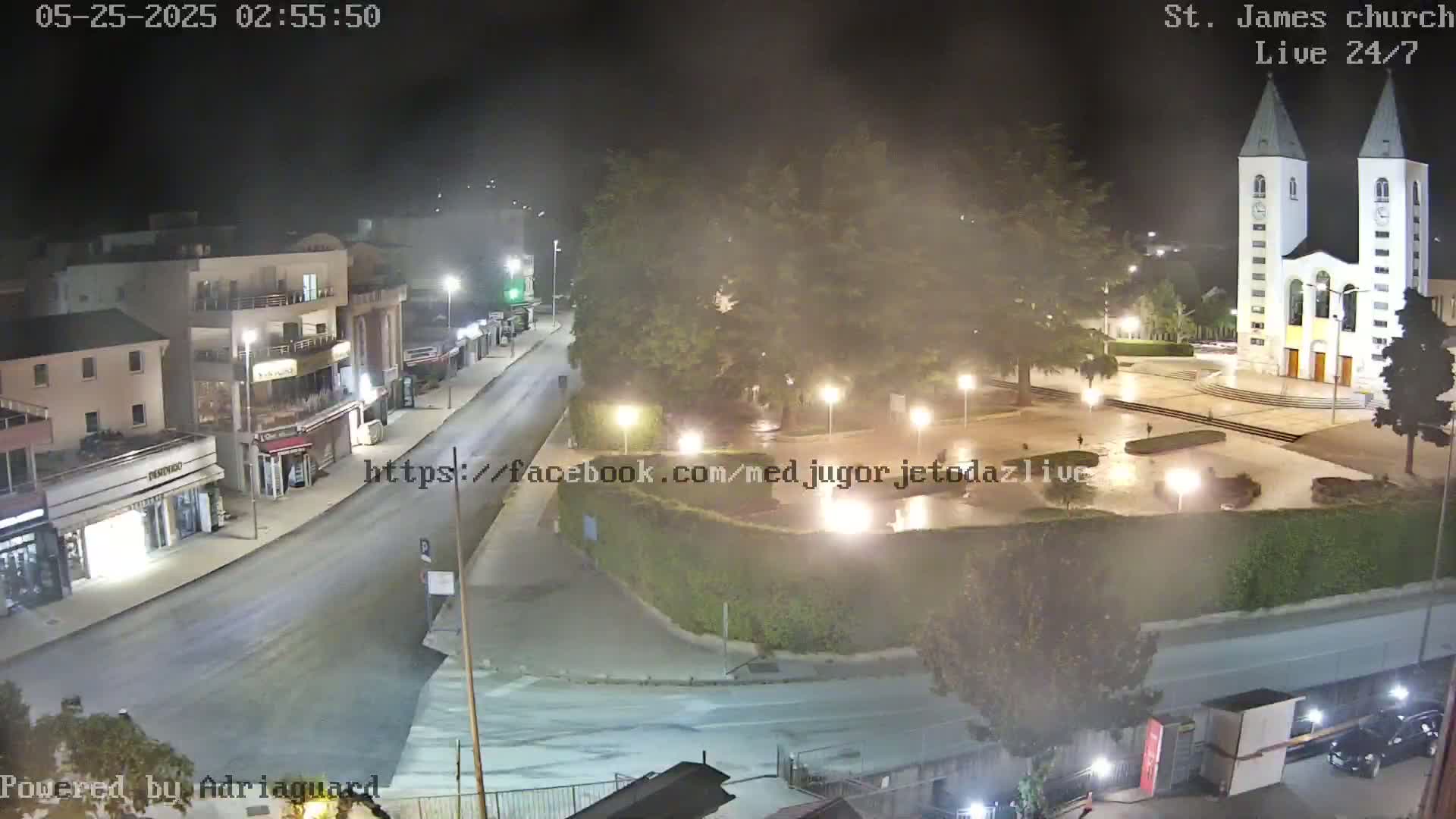A nighttime, slightly hazy view of a town square with a large church, buildings lining a street, and a few people visible.