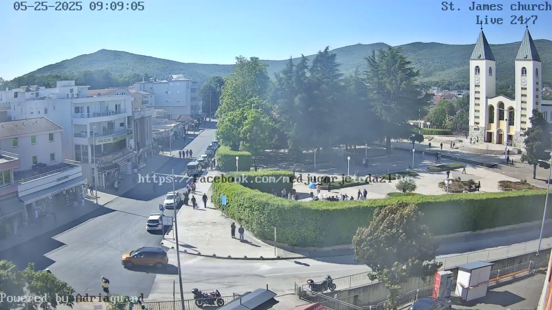 A town square with a church, surrounded by buildings and trees, on a sunny day.