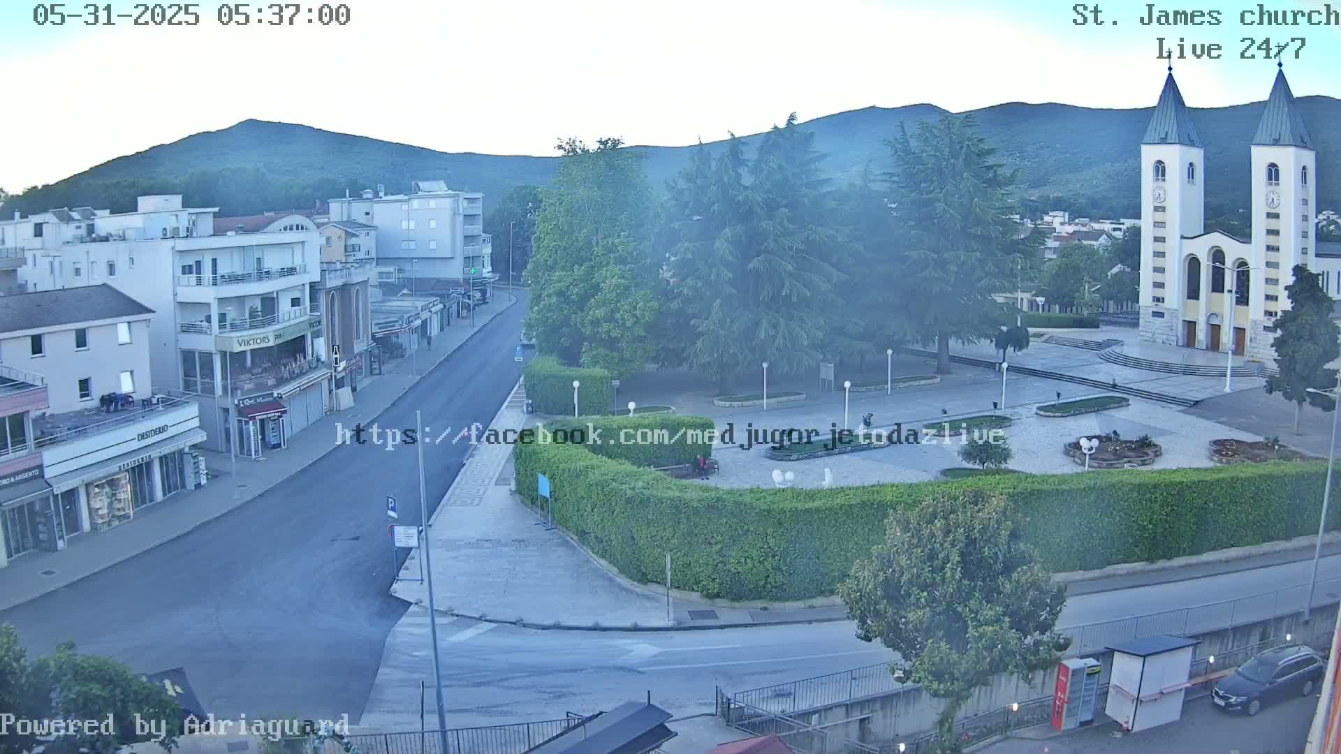 A hazy, early-morning view of a town square features a white church with twin spires, several buildings, and a street.