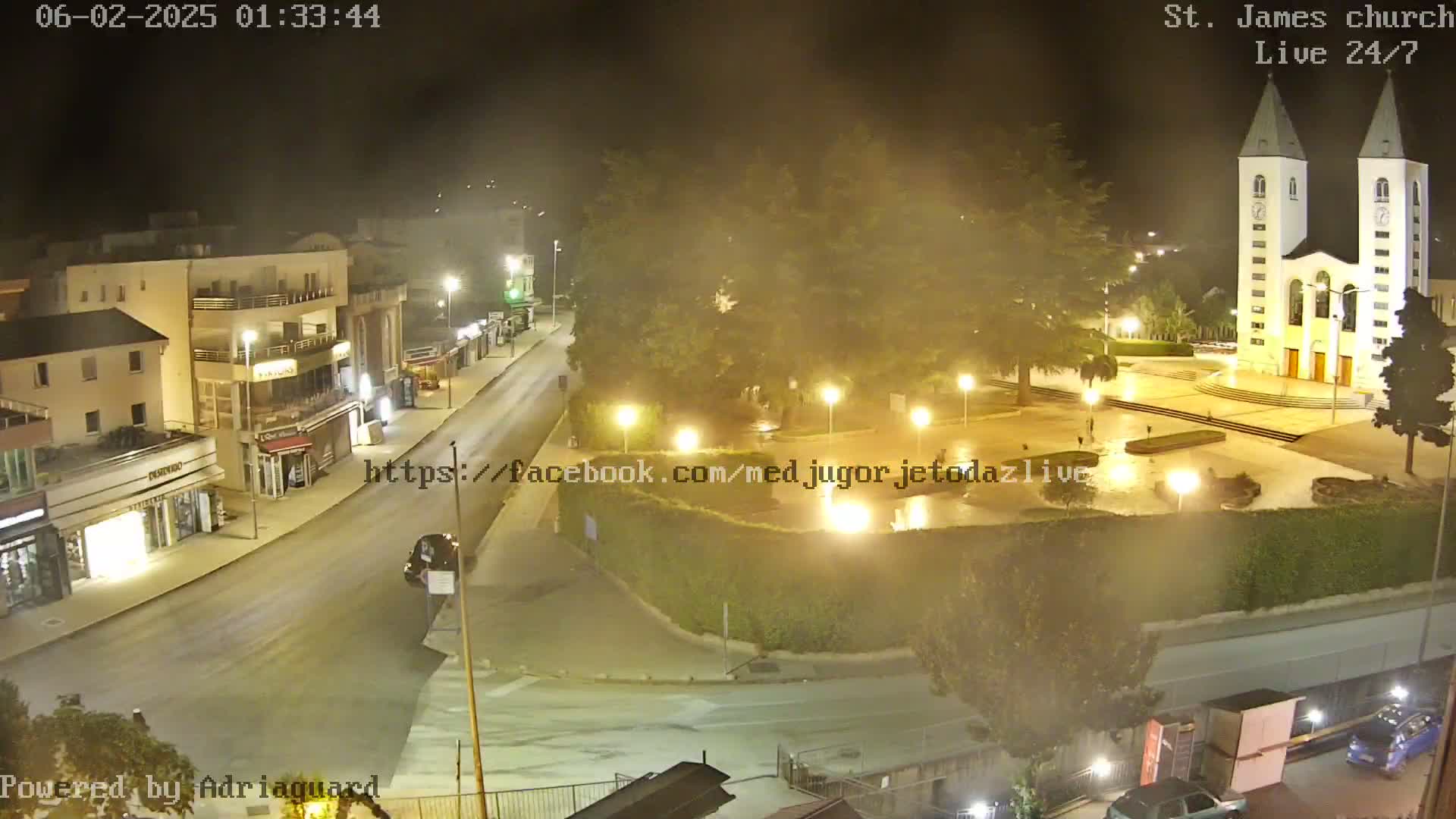 A nighttime, hazy view of a town square with a church, buildings, and a street.