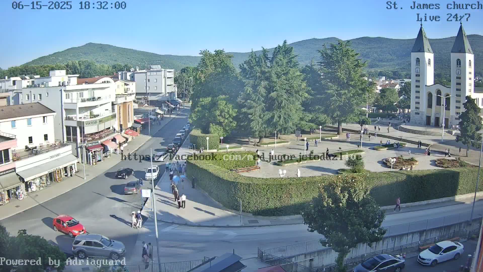 A high-angle, long shot of a town square on a sunny day, featuring a large church, surrounding buildings, and people walking around.