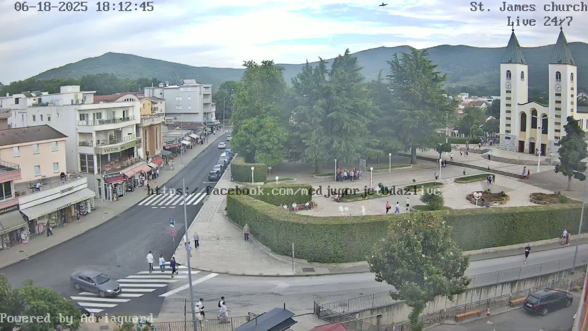 A town square with a church, shops, and people walking around under a partly cloudy sky.