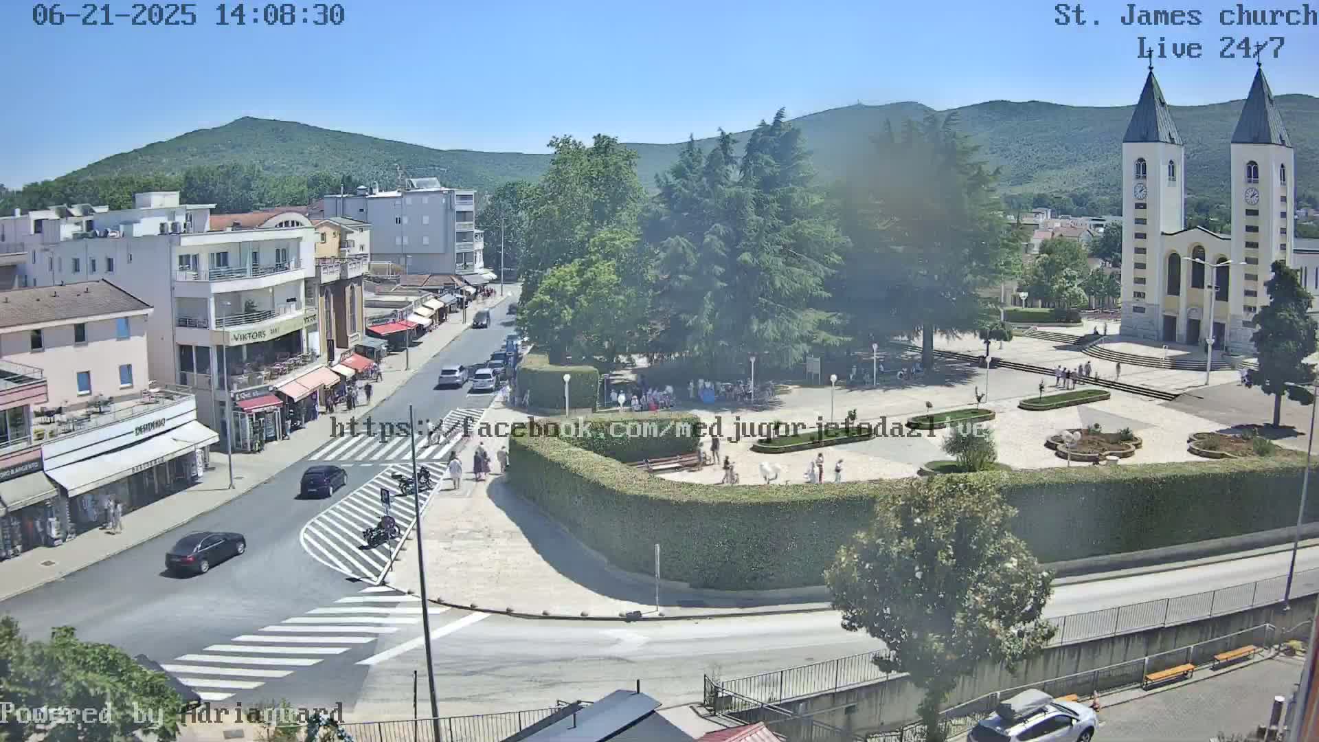 A sunny, aerial view shows a town square with a church, surrounding buildings, and cars on a street.