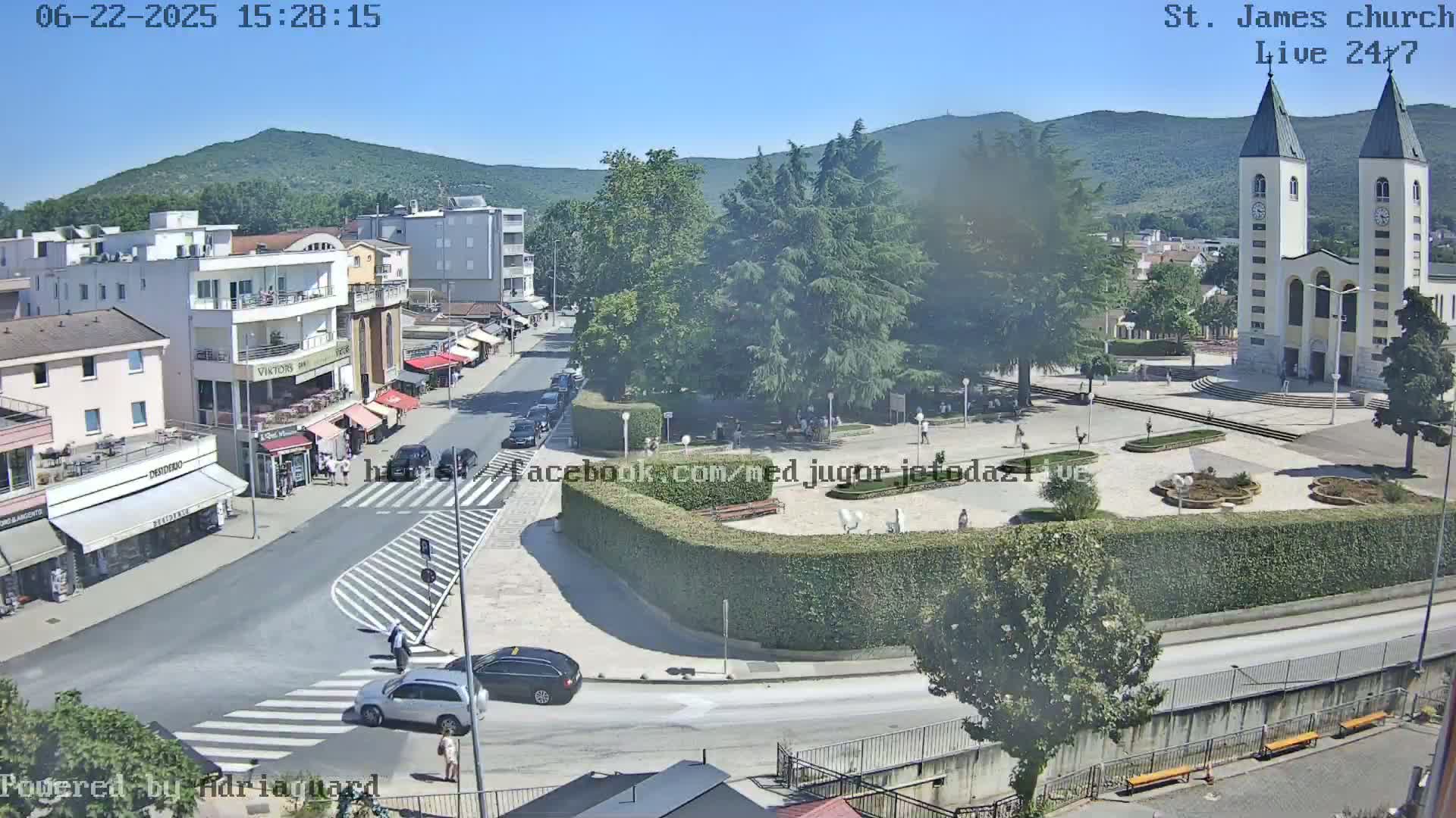 A sunny town square with a large church and surrounding buildings, viewed from above.
