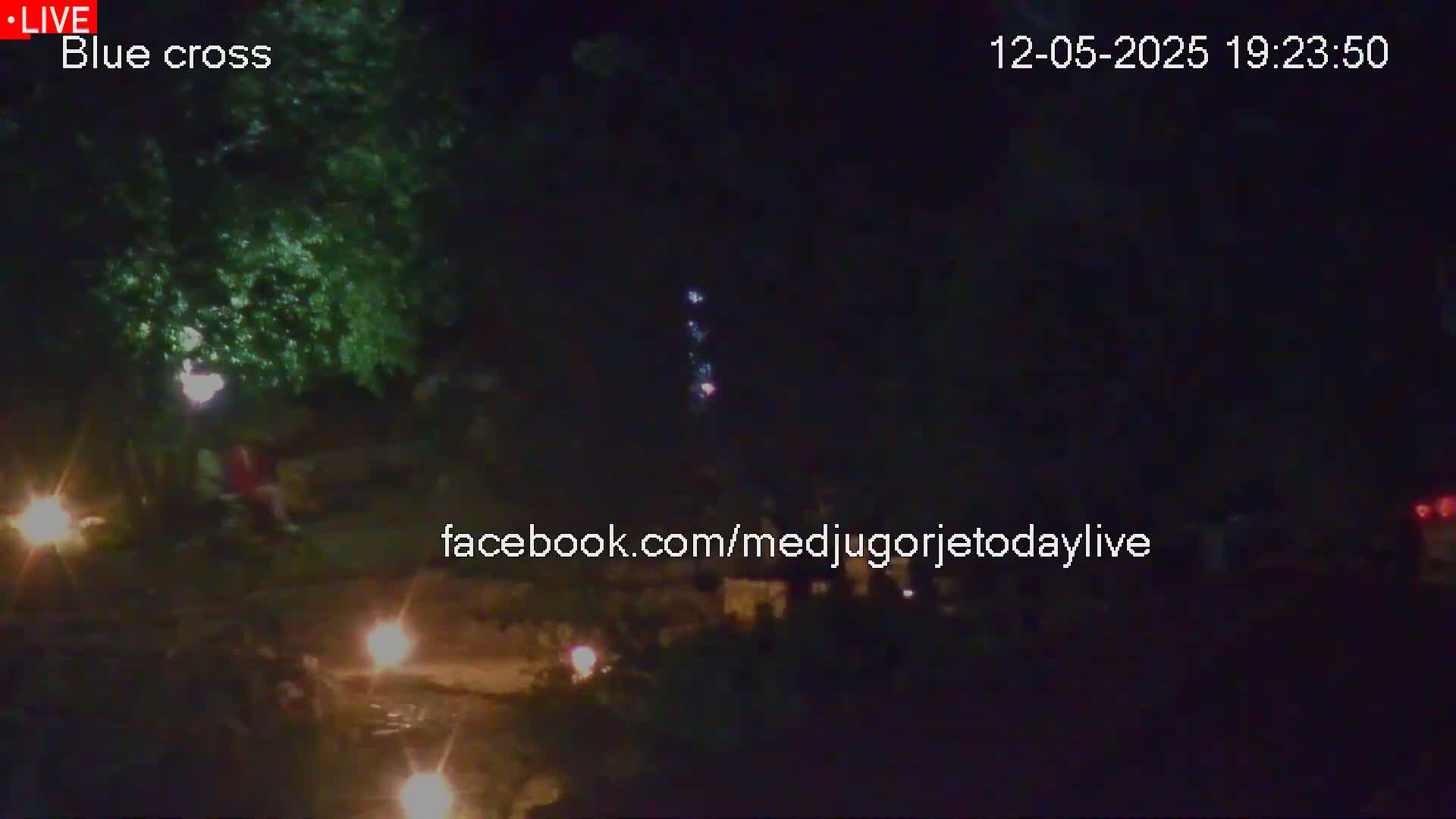 At night, a dark scene shows several people sitting near some small, flickering lights and a larger, distant light source, possibly flames.