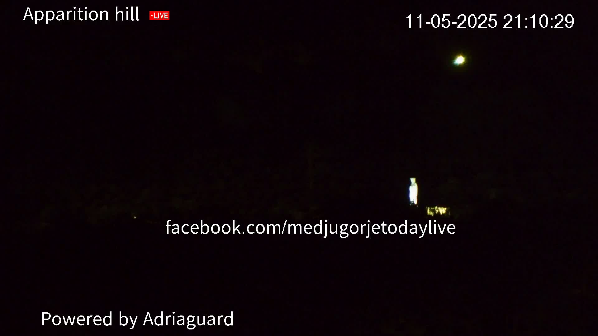 A dimly lit, nighttime scene shows a faintly glowing figure and a brighter light in the dark sky.