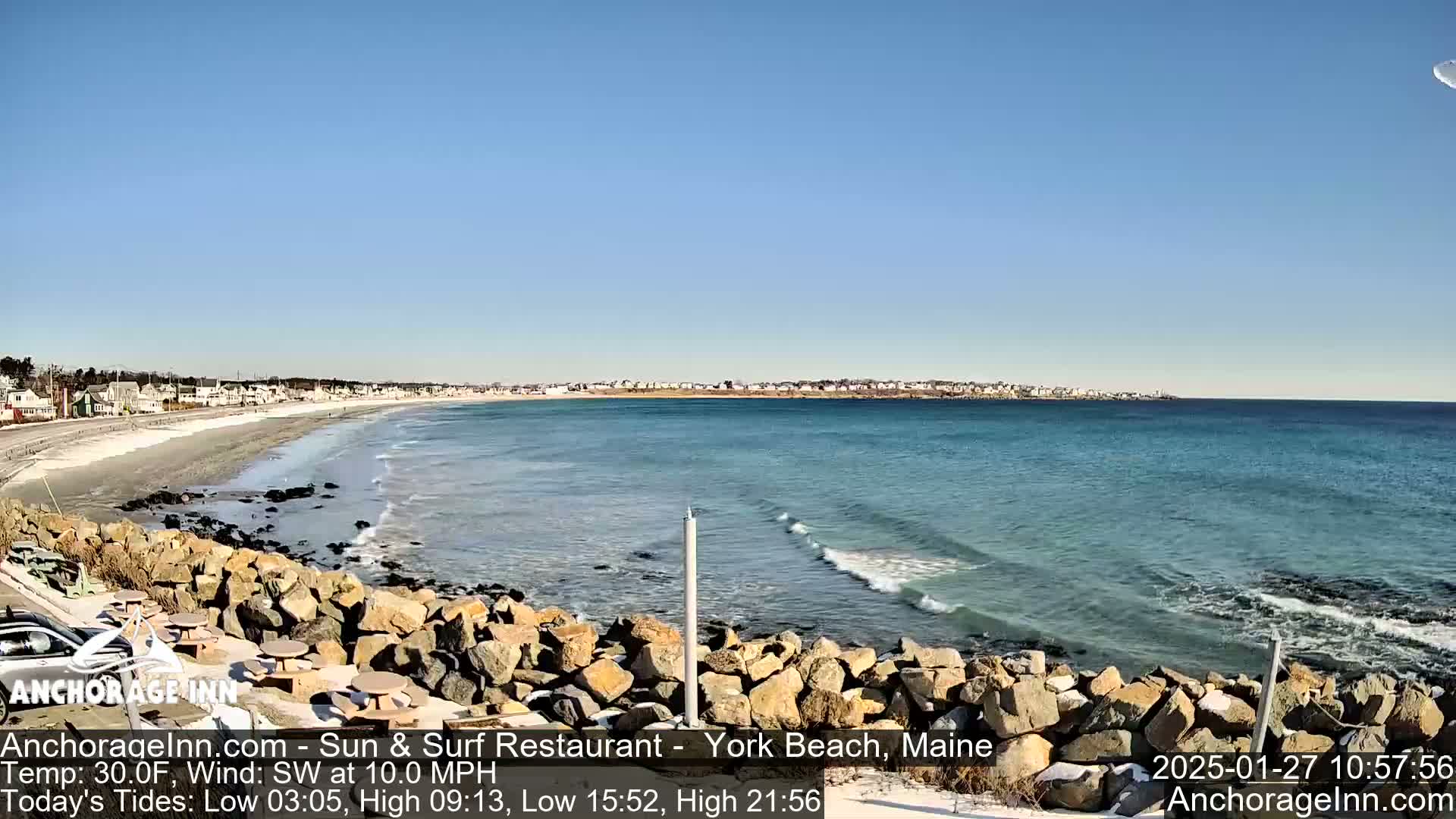 A sandy beach with a rocky shoreline and calm ocean waves stretches out under a clear blue sky.