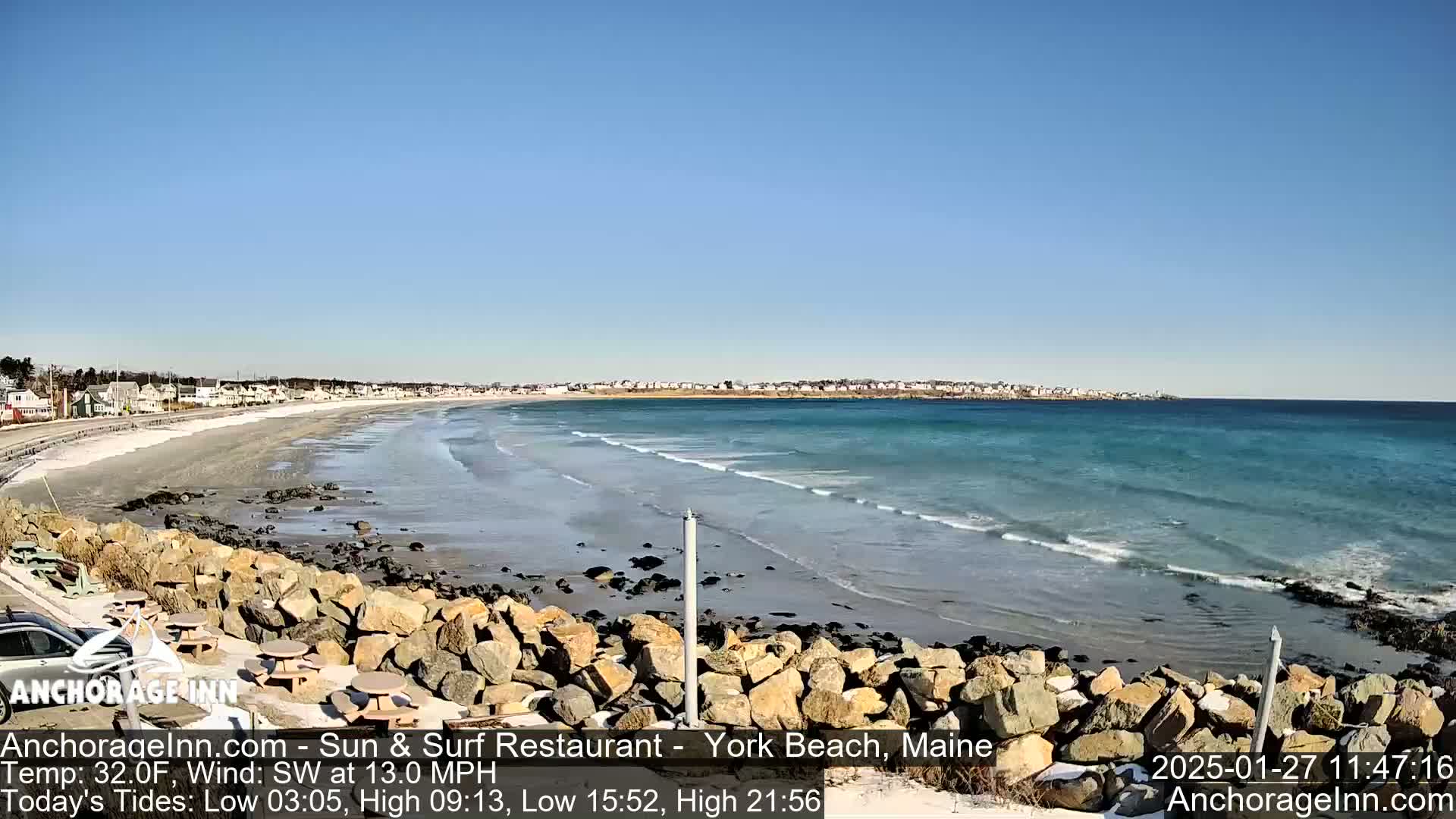 A sandy beach with a rocky shoreline meets a calm, turquoise ocean under a clear blue sky.
