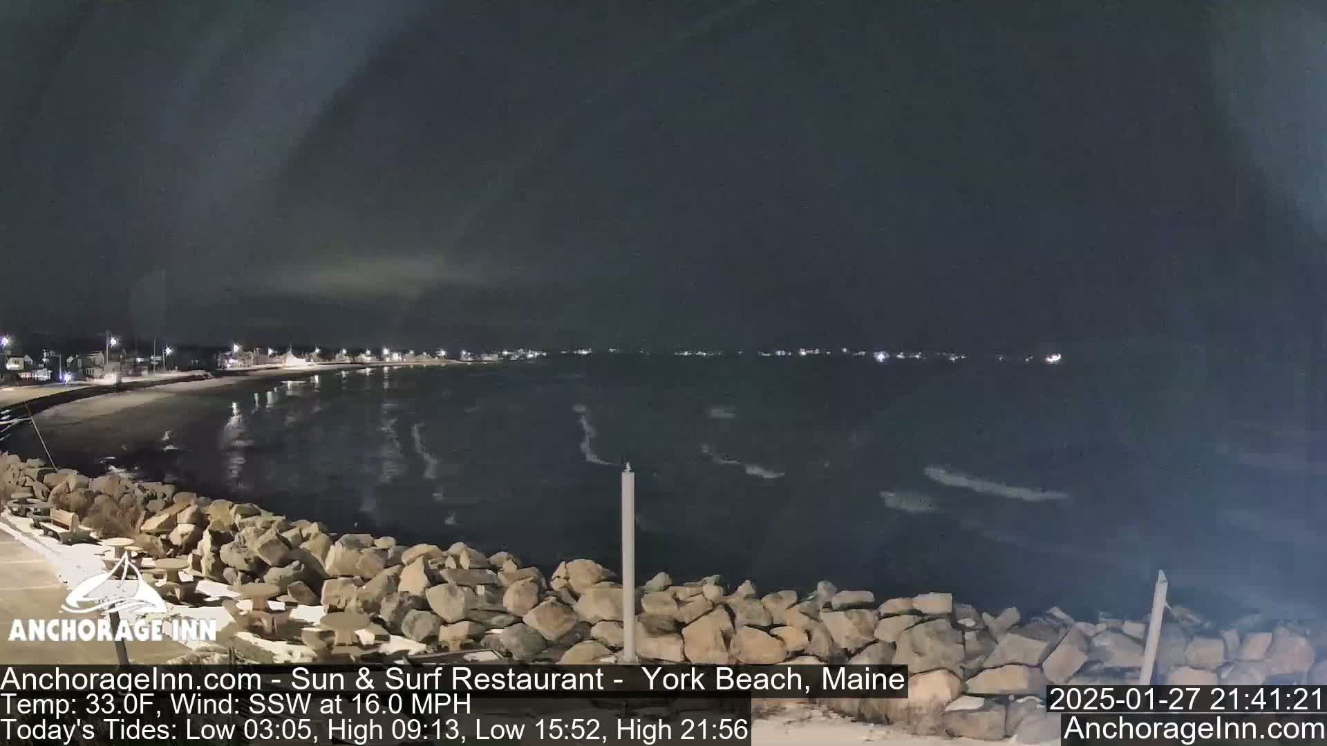A nighttime view of a rocky shoreline and calm ocean under a dark sky.