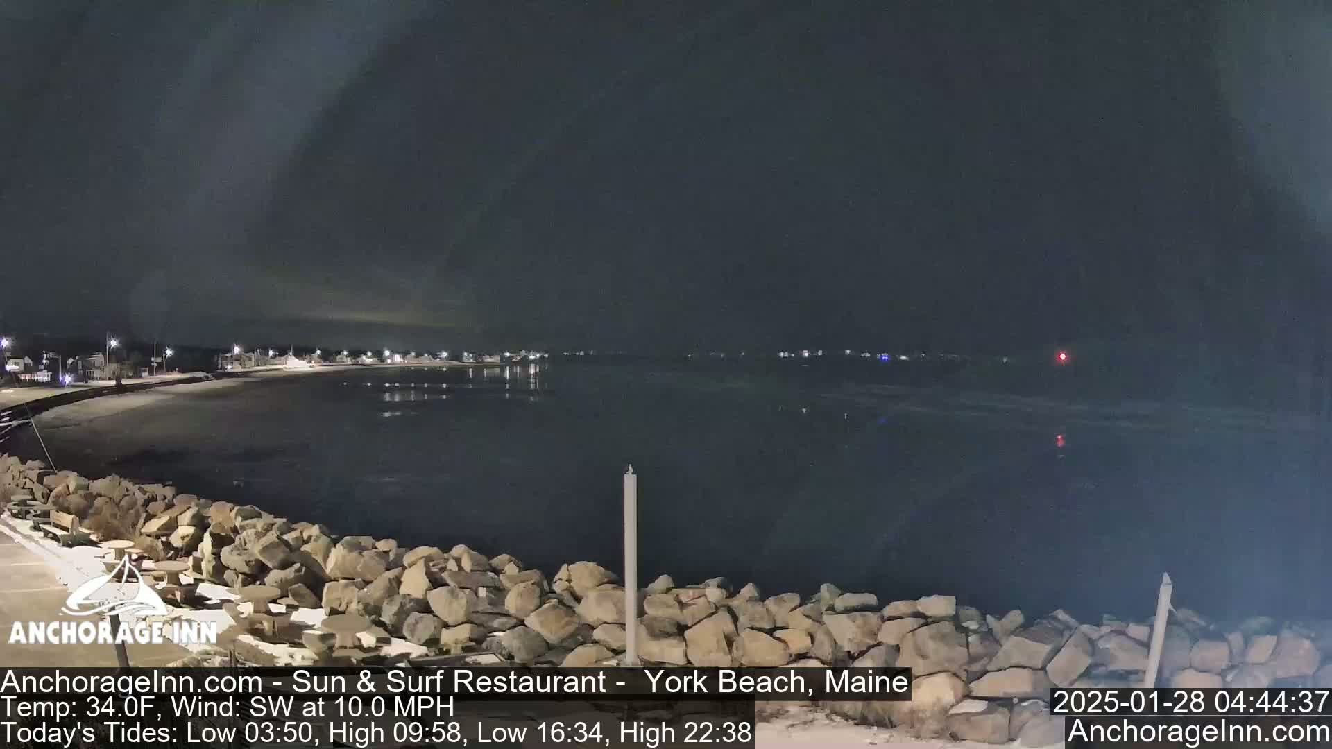 A nighttime view of a calm, dark body of water with a rocky shoreline under a dark, cloudy sky.