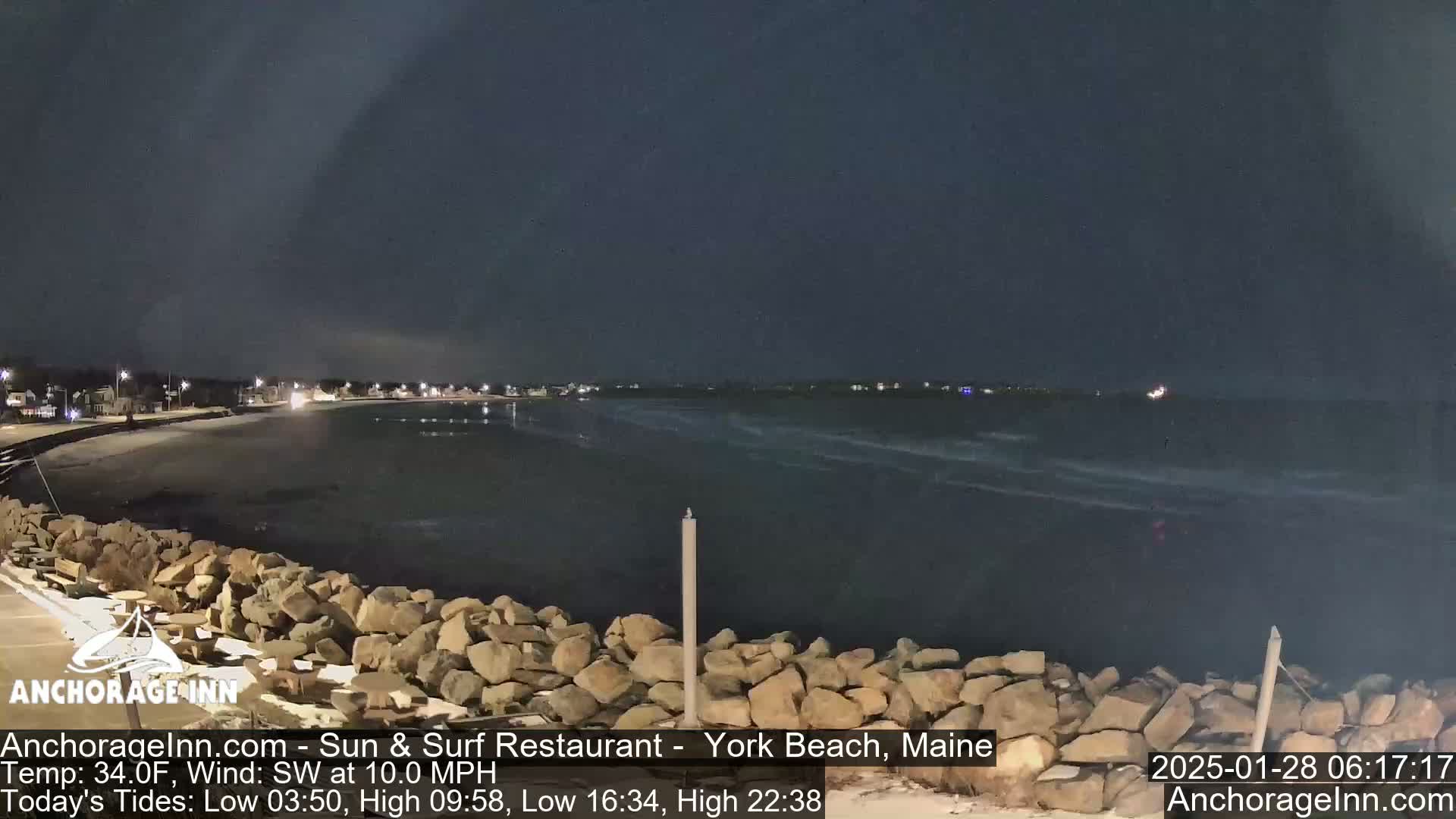 A nighttime view of a dark, wavy ocean meeting a rocky shoreline under a clear, dark sky.