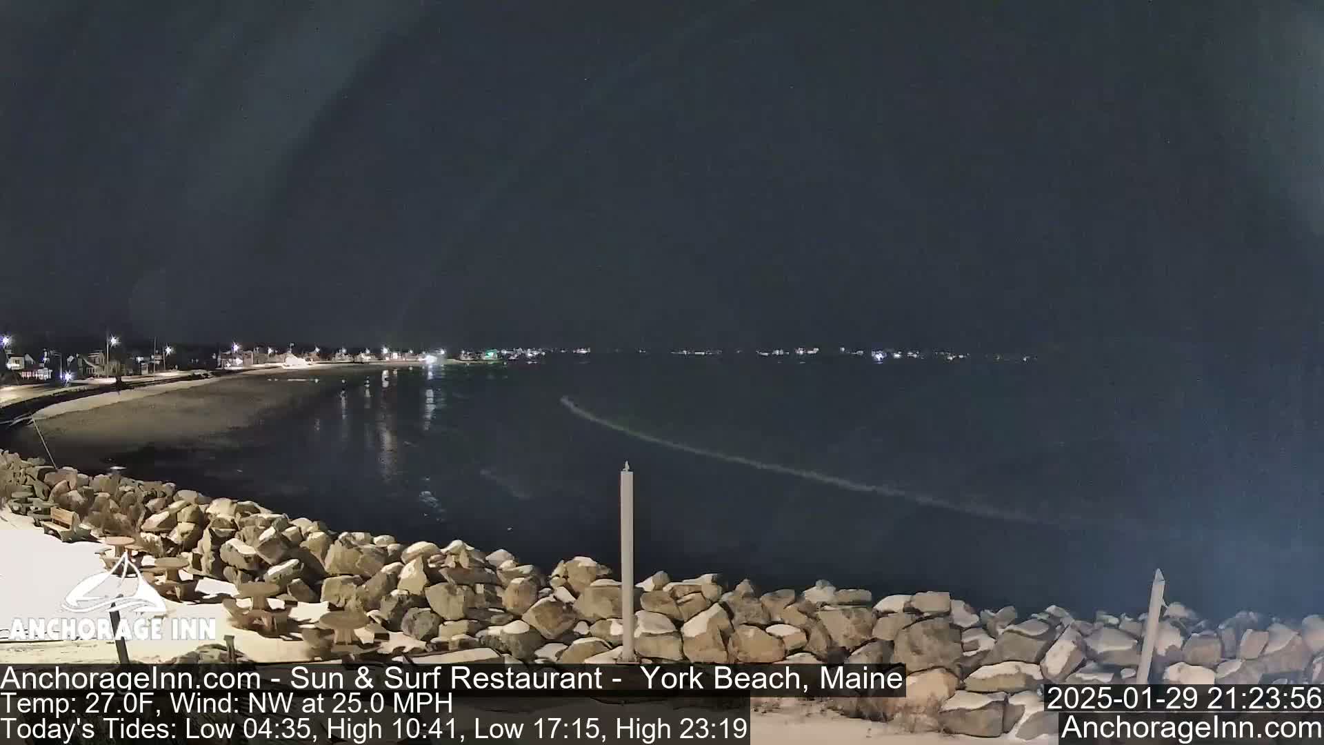 A nighttime view of a rocky shoreline and calm ocean under a dark sky.