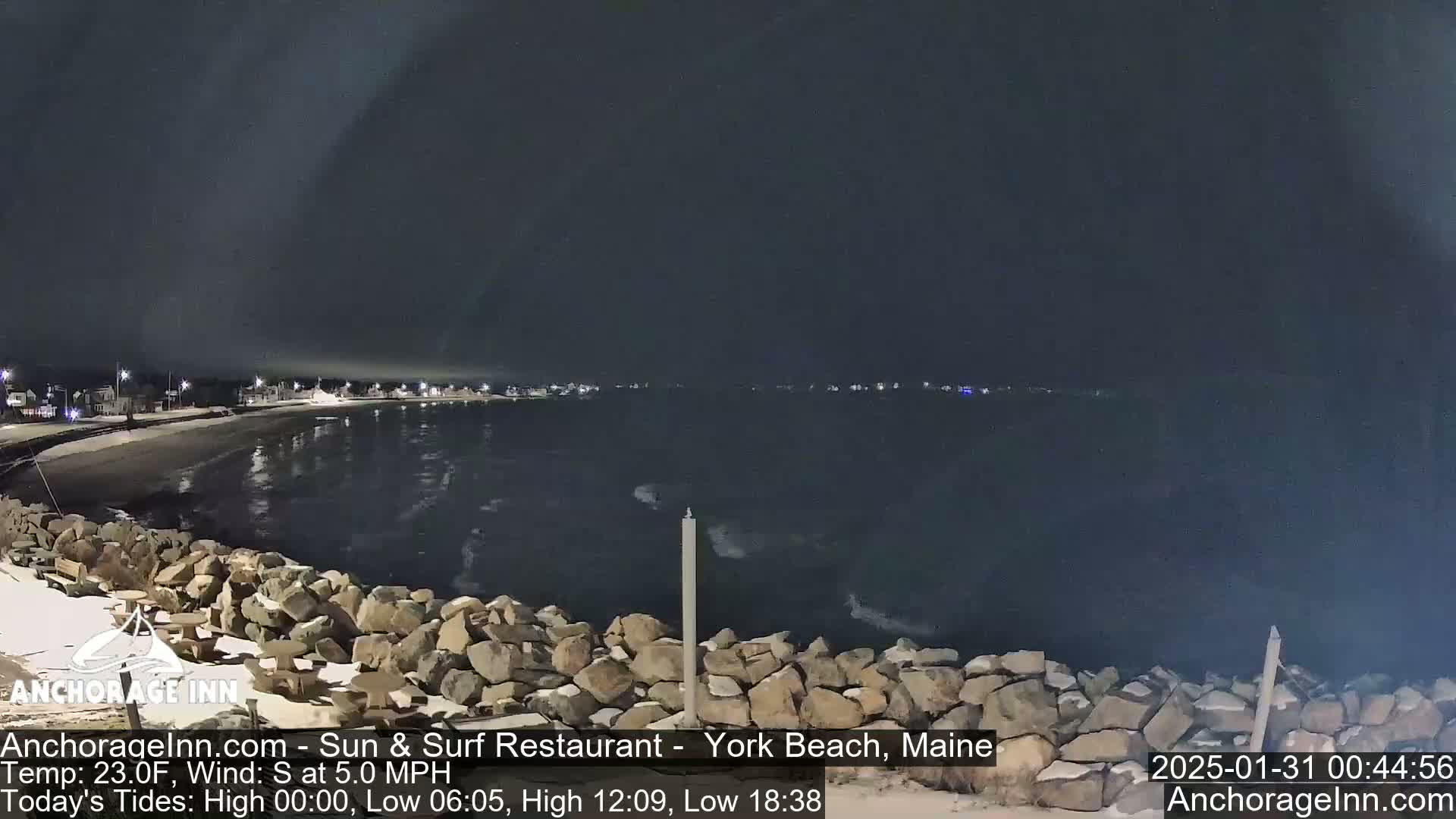 A nighttime view of a rocky shoreline and calm ocean under a dark sky.