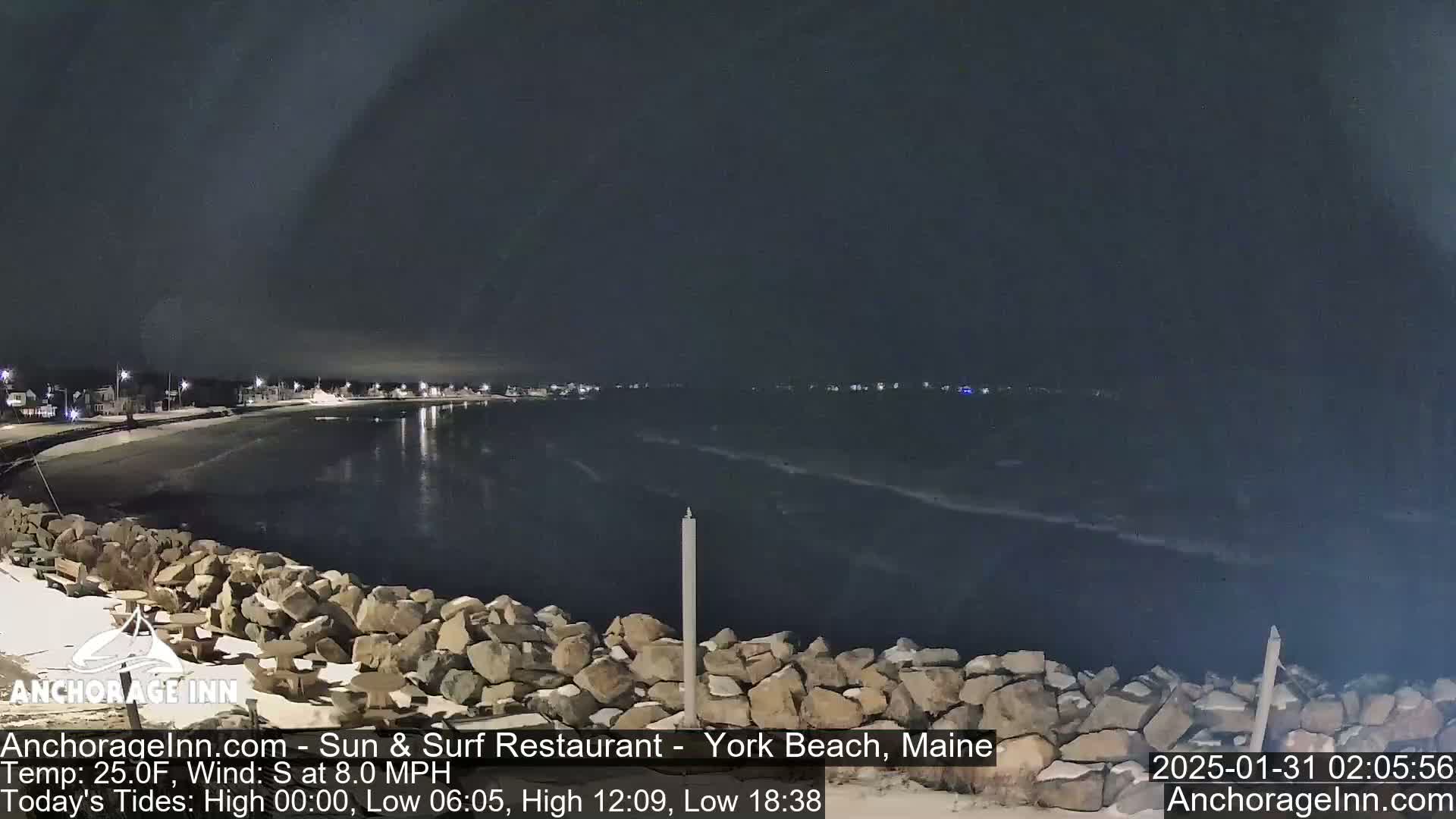 A nighttime view of a rocky shoreline and calm ocean under a dark sky.
