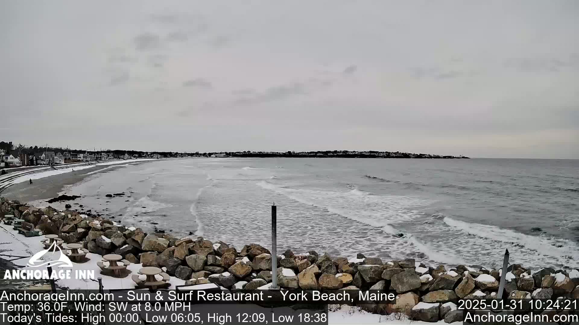 A snow-dusted rocky shoreline overlooks a grey ocean with small waves under an overcast sky.