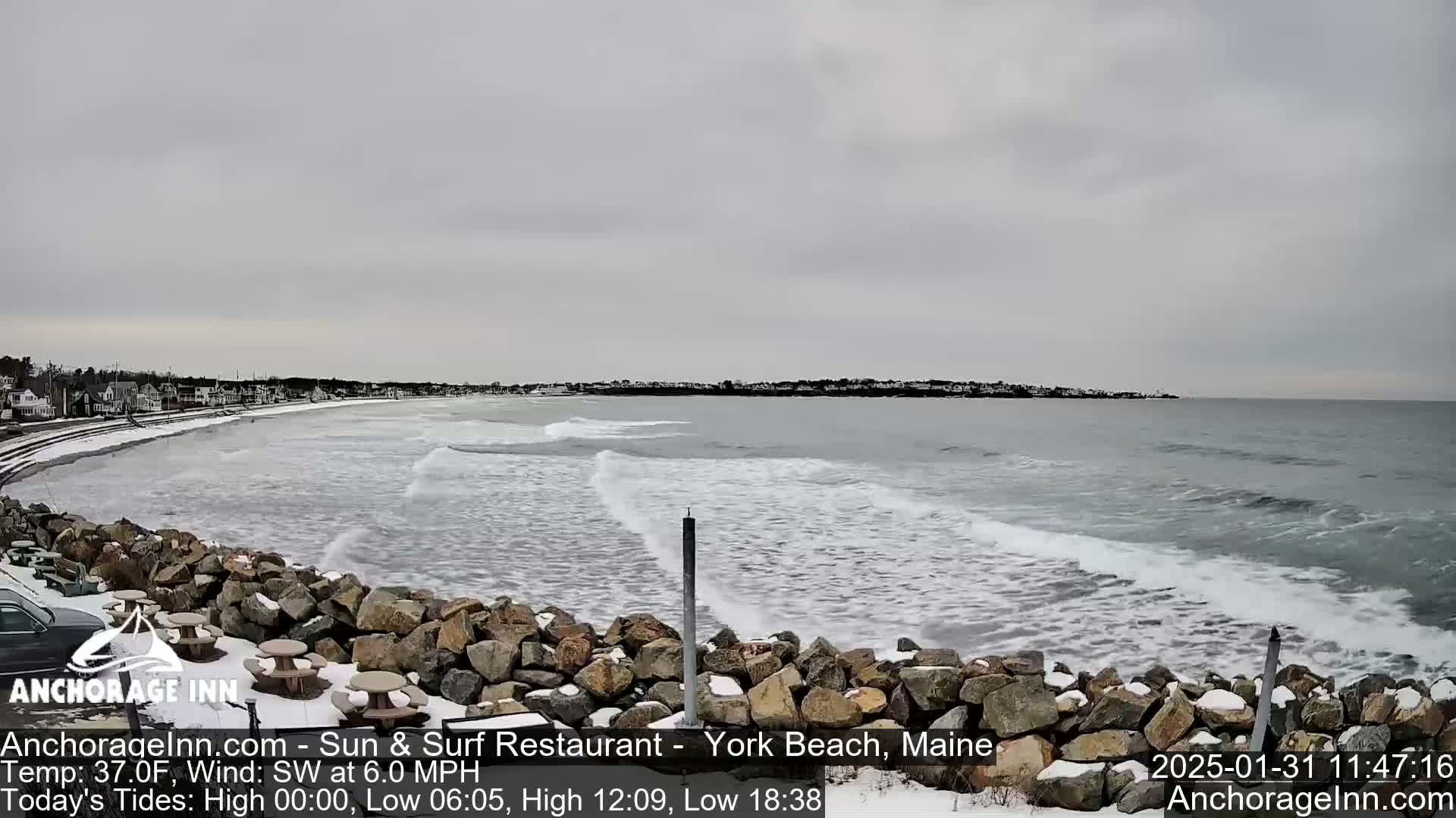 A snow-dusted rocky shoreline overlooks a gray, wavy ocean under an overcast sky.